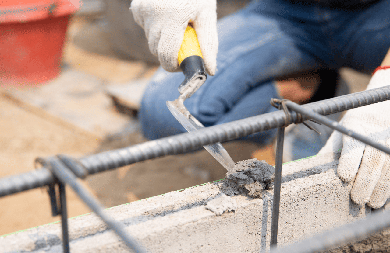 Stone Haven Developments A person wearing white gloves uses a trowel to apply wet cement to a concrete surface with exposed steel reinforcement bars. Ontario