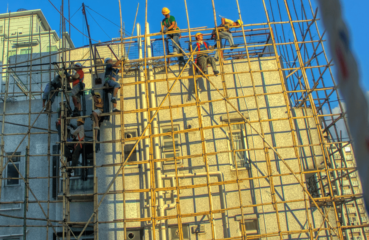 Stone Haven Developments Construction workers assembling bamboo scaffolding on the exterior of a multi-story building under clear blue skies. Ontario