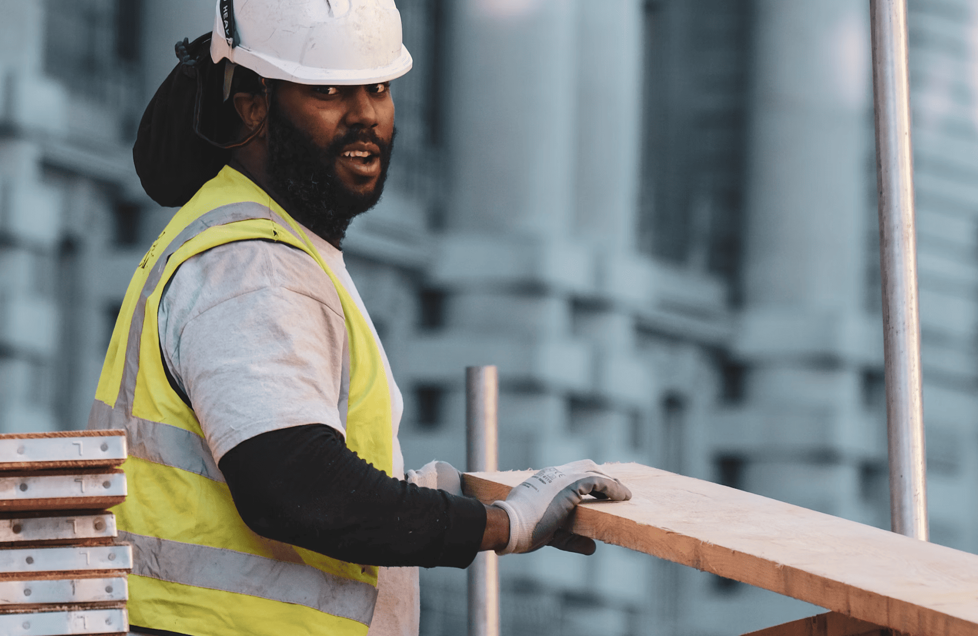 Stone Haven Developments A construction worker wearing a white hard hat, yellow safety vest, and gloves holds a wooden plank at a building site. Ontario