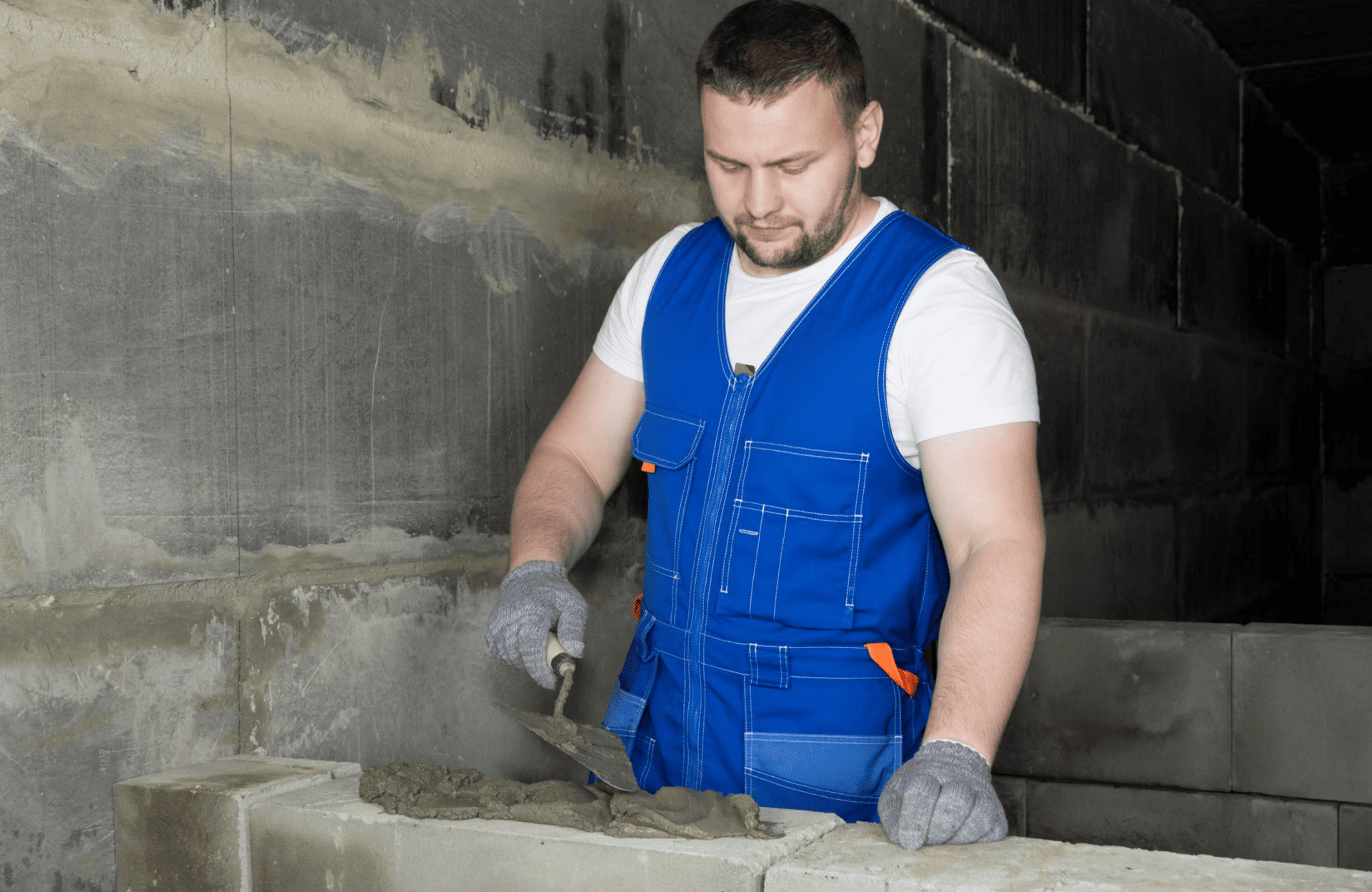 Stone Haven Developments A construction worker in a blue vest spreads mortar on concrete blocks with a trowel inside an unfinished building. Ontario