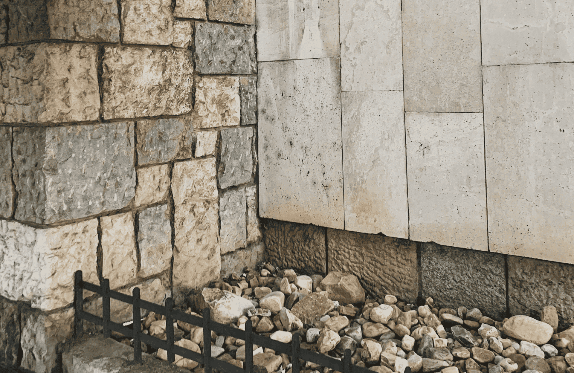 Stone Haven Developments A stone wall meets a tile wall at a corner, with rocks scattered on the ground below and a small black metal fence in the foreground. Ontario