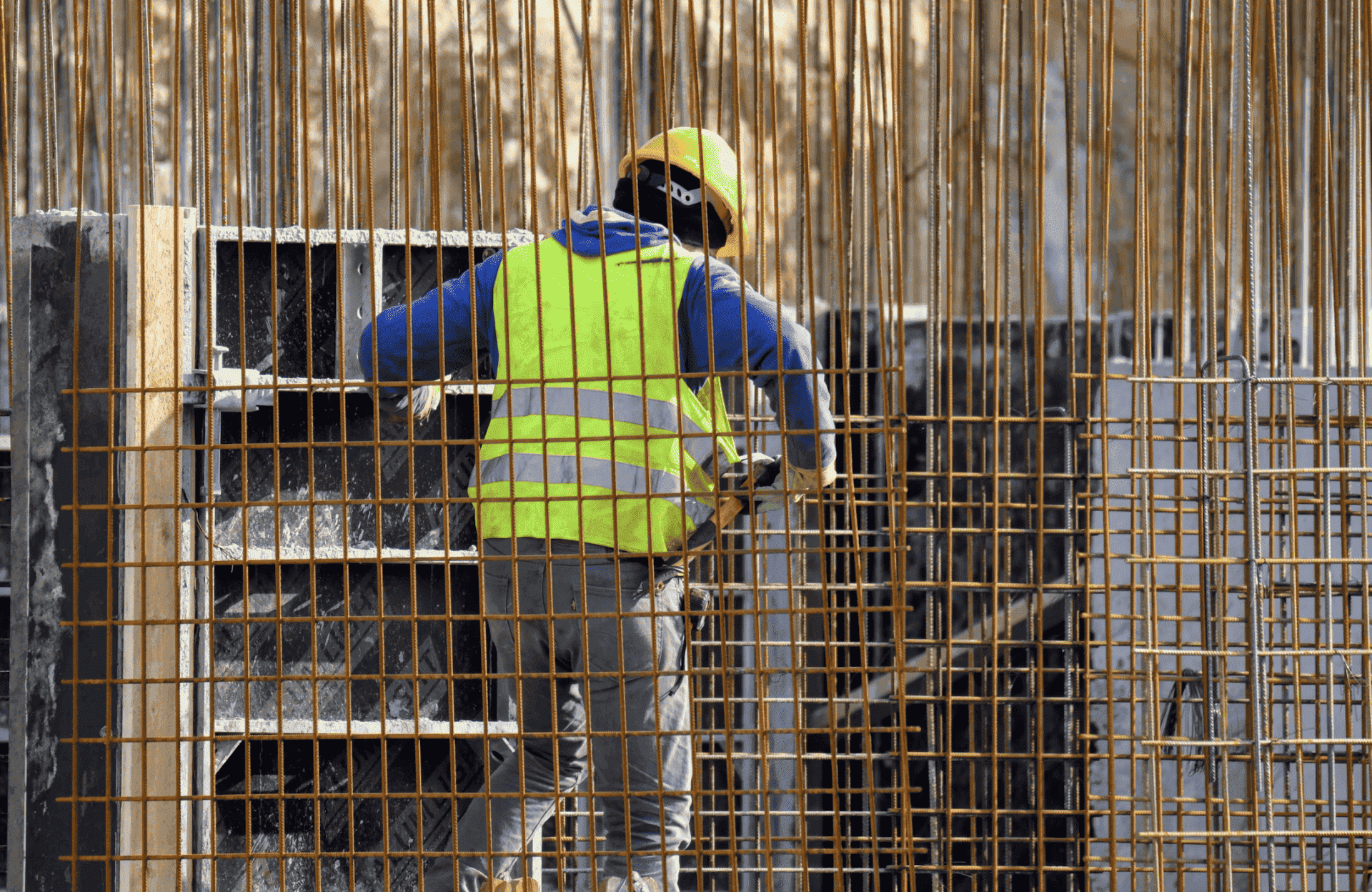 Stone Haven Developments A construction worker in a yellow safety vest and helmet stands among steel rebar, working on a building site. Ontario