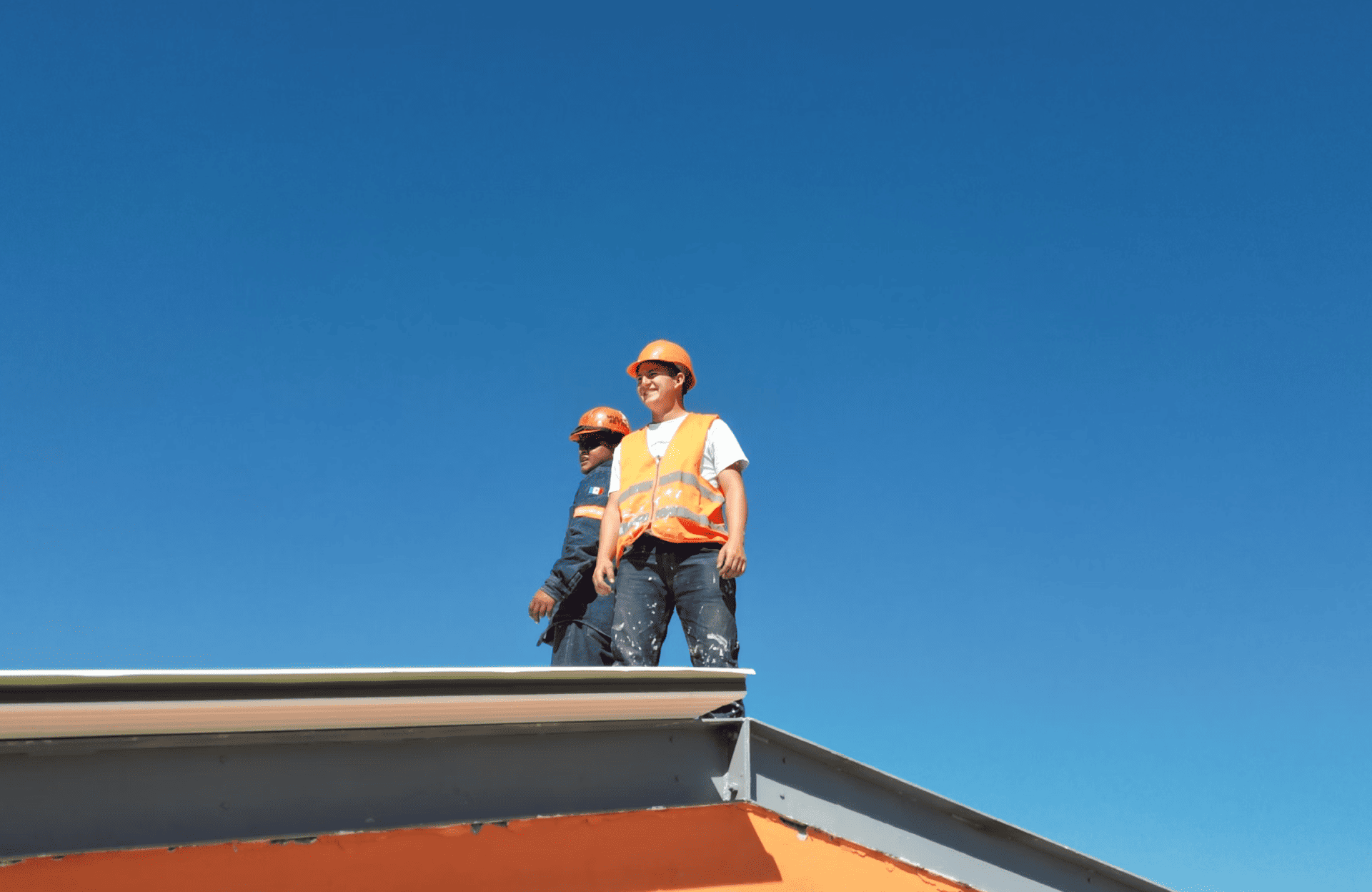 Stone Haven Developments Two construction workers wearing safety vests and helmets stand on a roof under a clear blue sky. Ontario