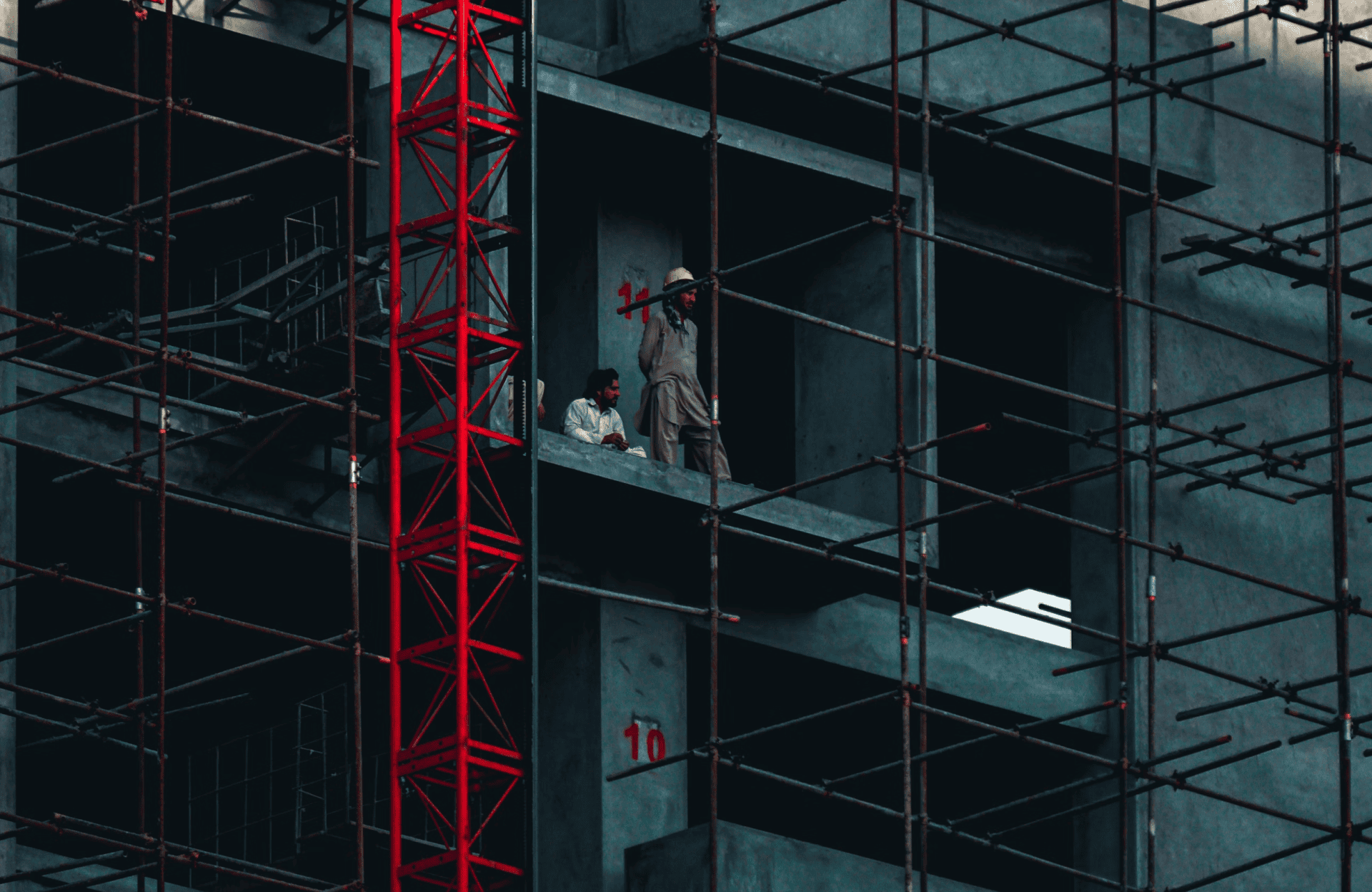 Stone Haven Developments Two construction workers stand on an unfinished floor of a building surrounded by metal scaffolding and a red structural framework. Ontario