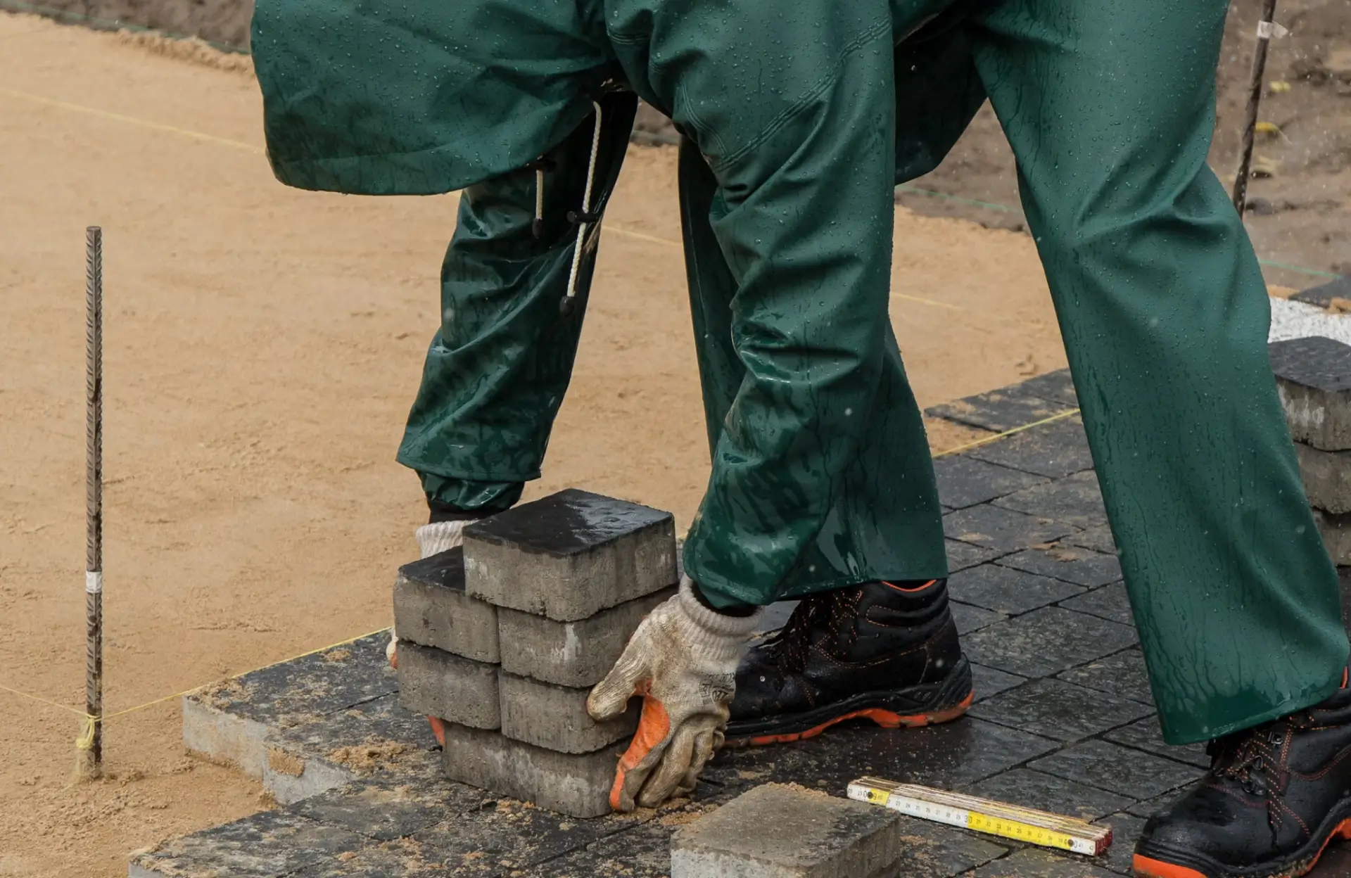 Stone Haven Developments A person in green rain gear and gloves is placing concrete pavers on the ground at a construction site. Ontario