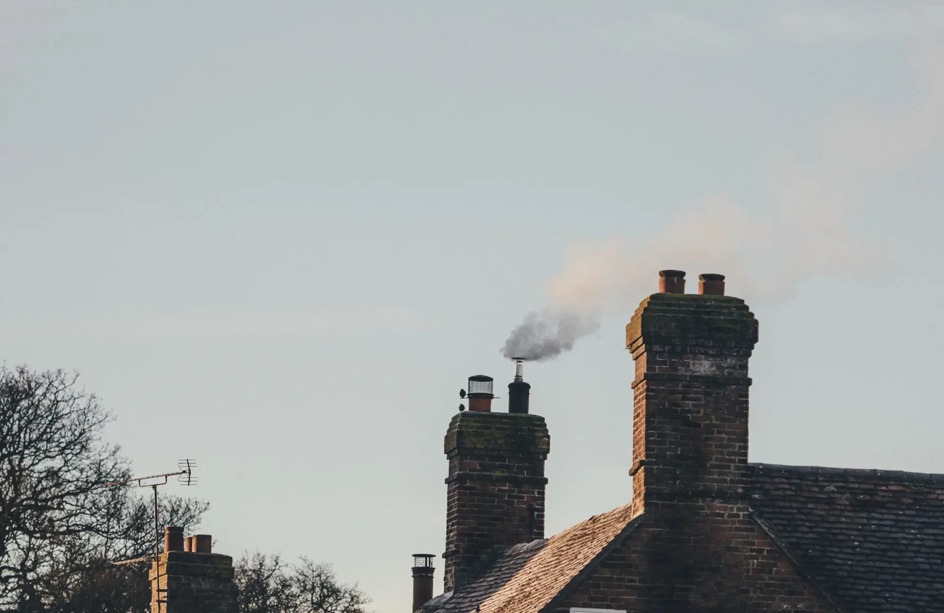 Stone Haven Developments Smoke rises from a chimney on a brick house roof under a clear sky, with trees partially visible in the background. Ontario