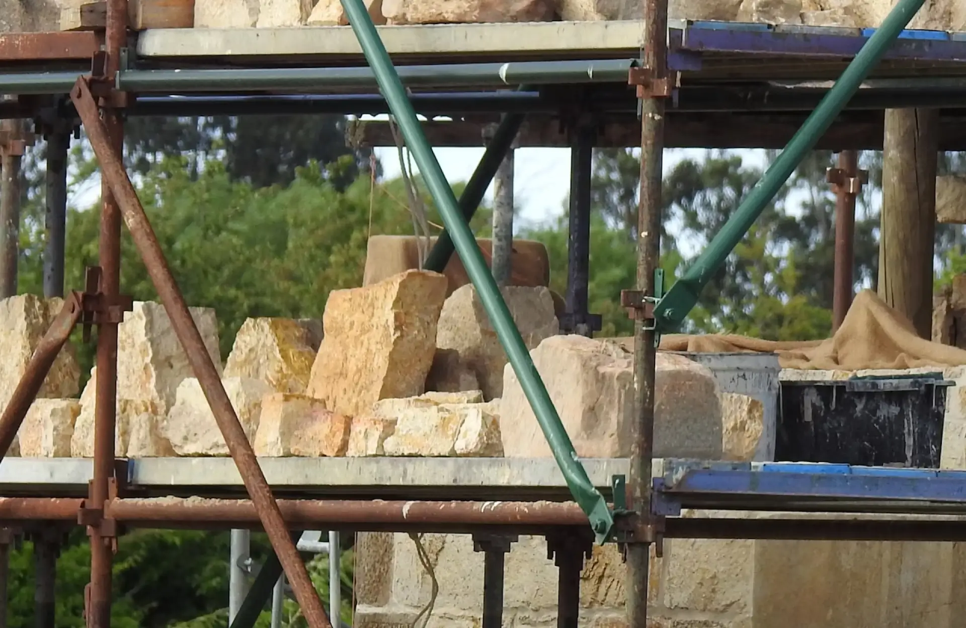 Stone Haven Developments A close-up view of scaffolding supporting stacked stone blocks at a construction site, with trees visible in the background. Ontario