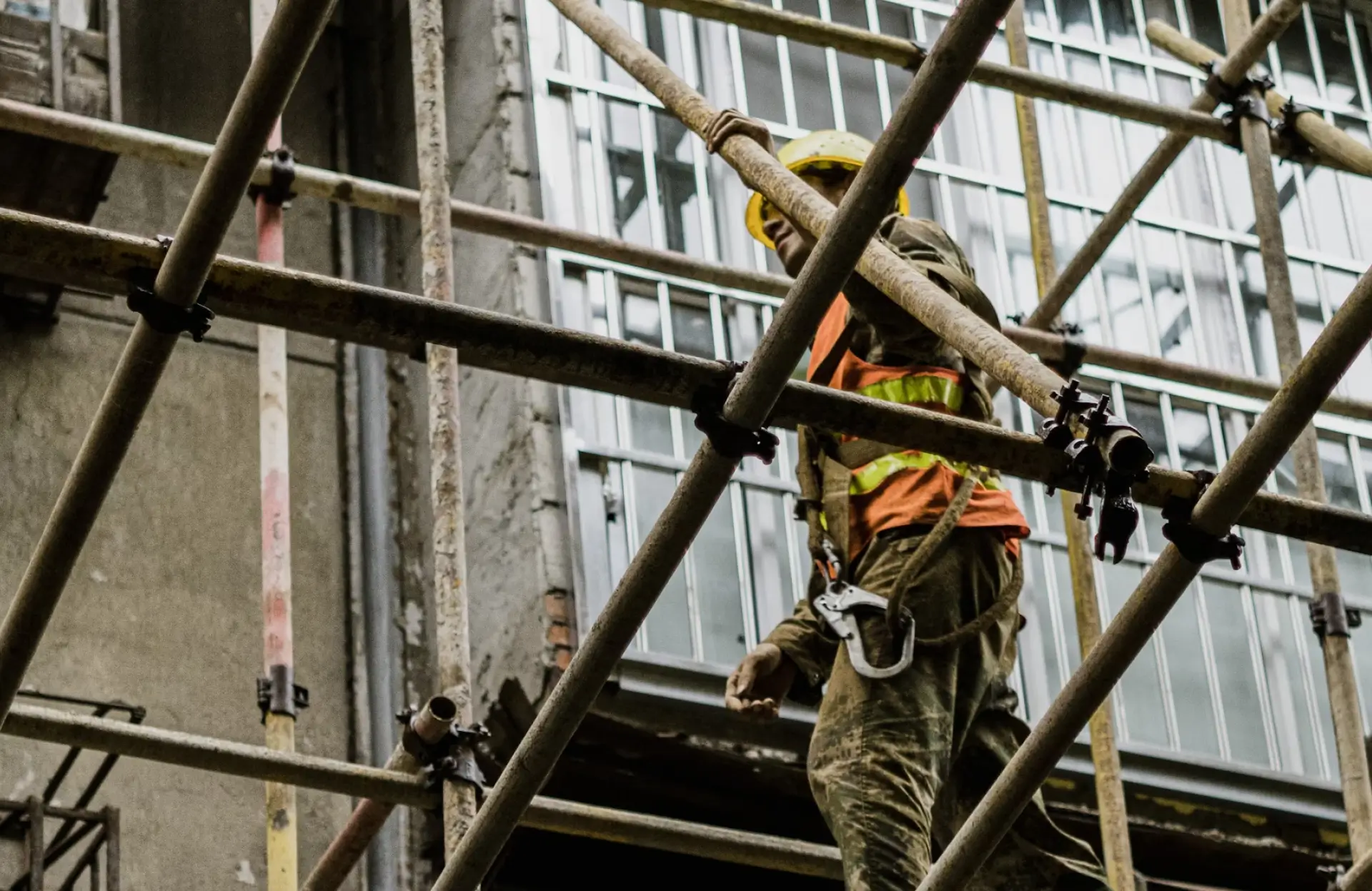 Stone Haven Developments Construction worker wearing safety gear stands on scaffolding in front of a building with large windows and exposed concrete. Ontario