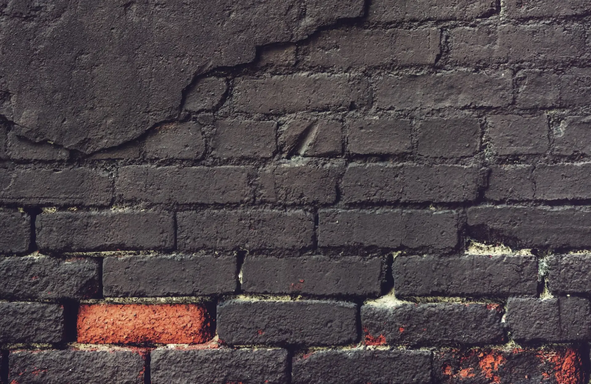 Stone Haven Developments A weathered brick wall with dark paint chipping off, revealing some exposed red bricks near the bottom. Ontario