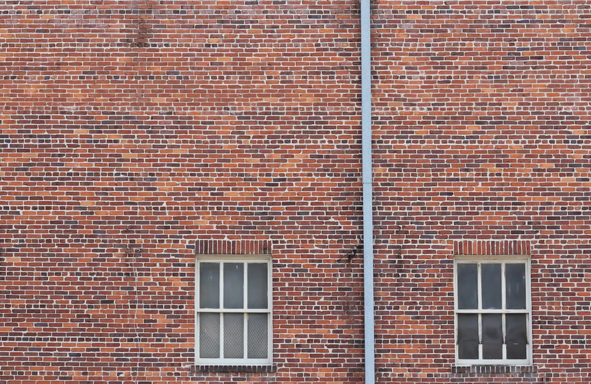 Stone Haven Developments A brick wall with two identical rectangular windows at the bottom and a vertical metal pipe running between them. Ontario