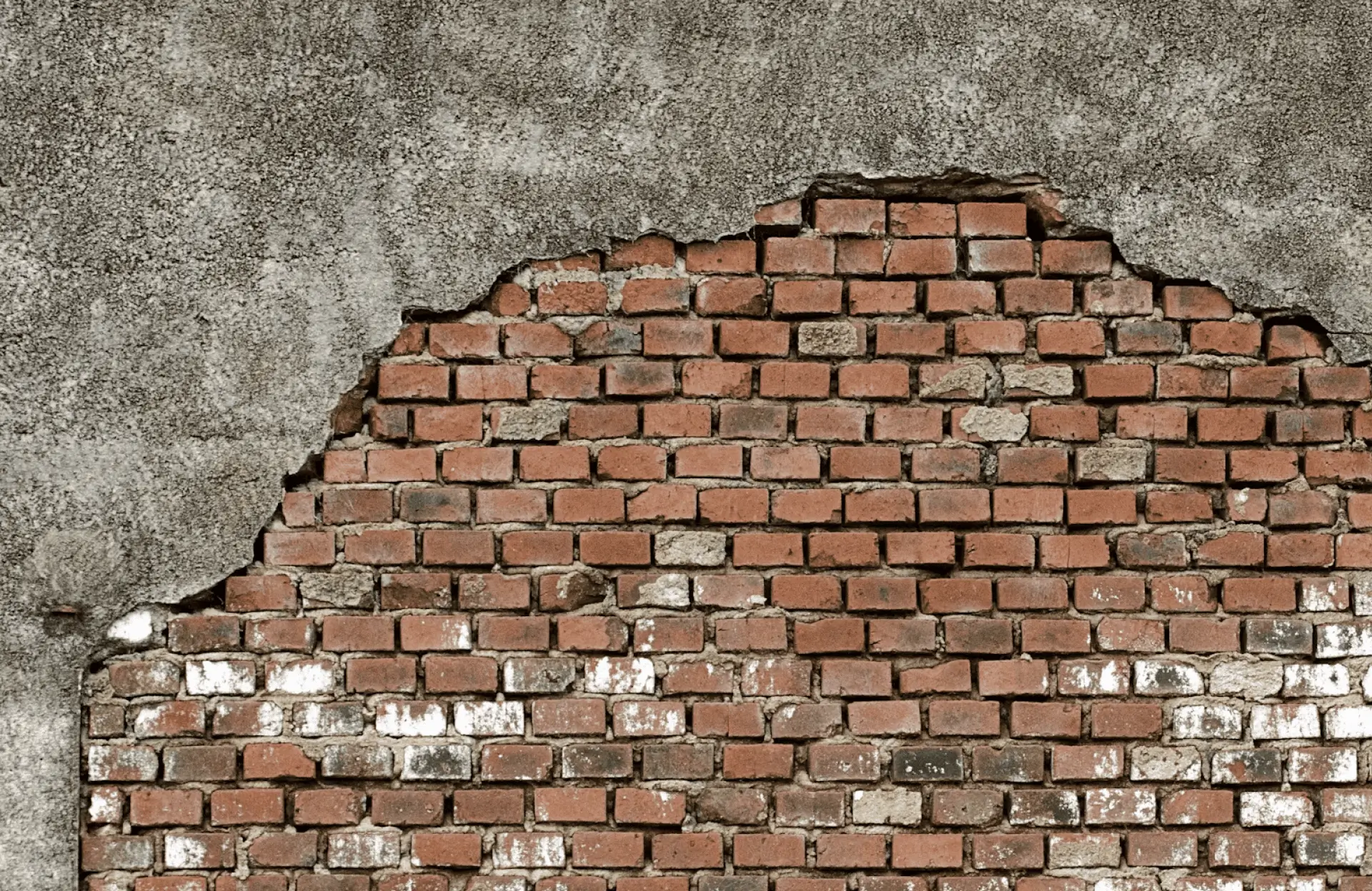 Stone Haven Developments A partially exposed brick wall with crumbling gray plaster, revealing red bricks underneath. Some bricks are stained with white patches. Ontario custom masonry services.