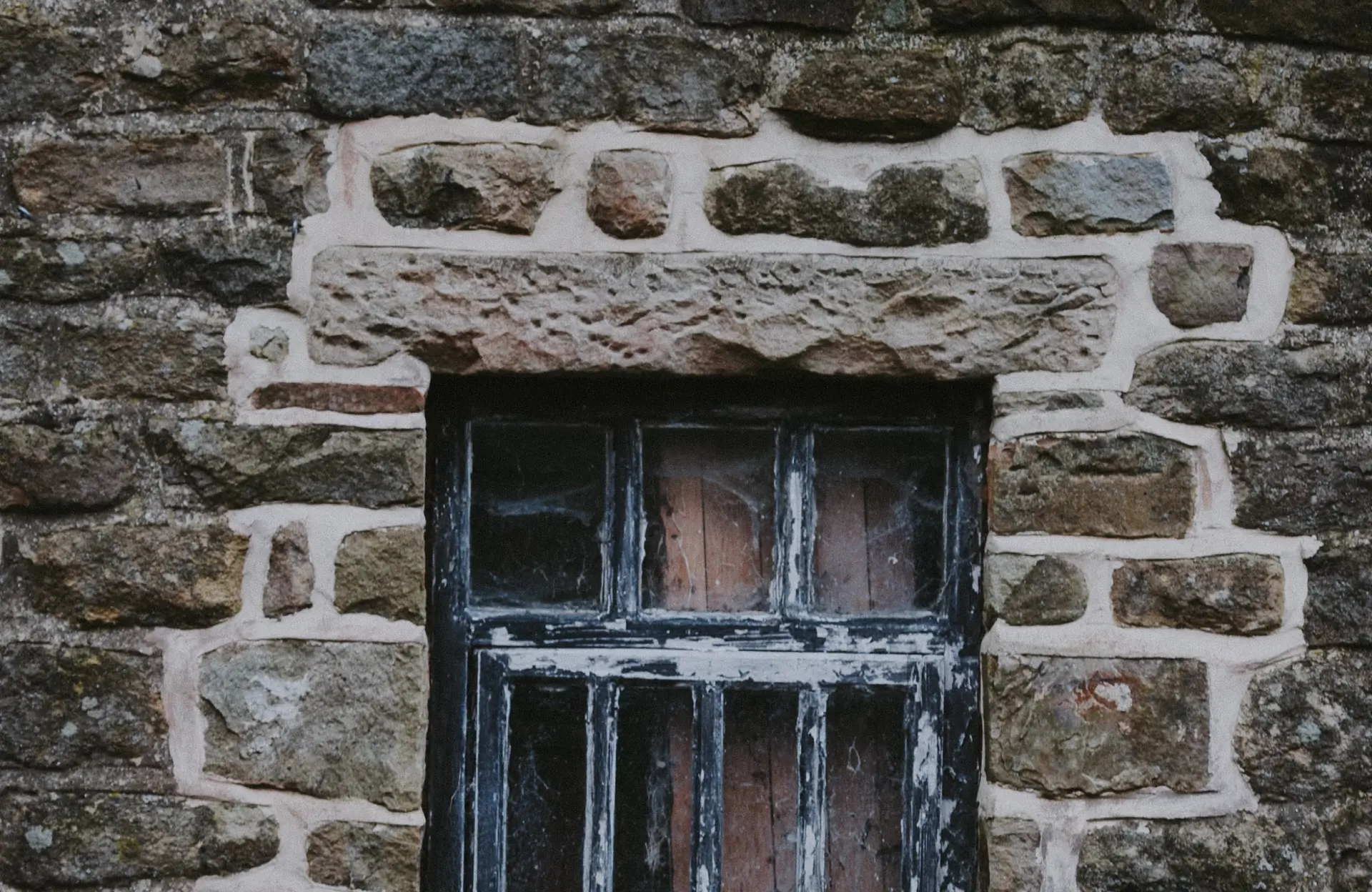 Stone Haven Developments A close-up of a small, old window with peeling paint set in a stone wall. Ontario