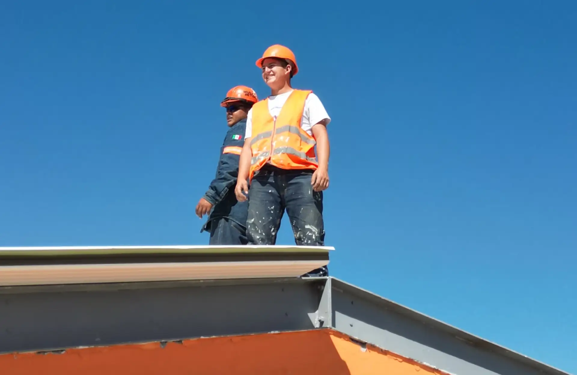 Stone Haven Developments Two construction workers wearing orange safety helmets and vests stand on a roof under a clear blue sky. Ontario