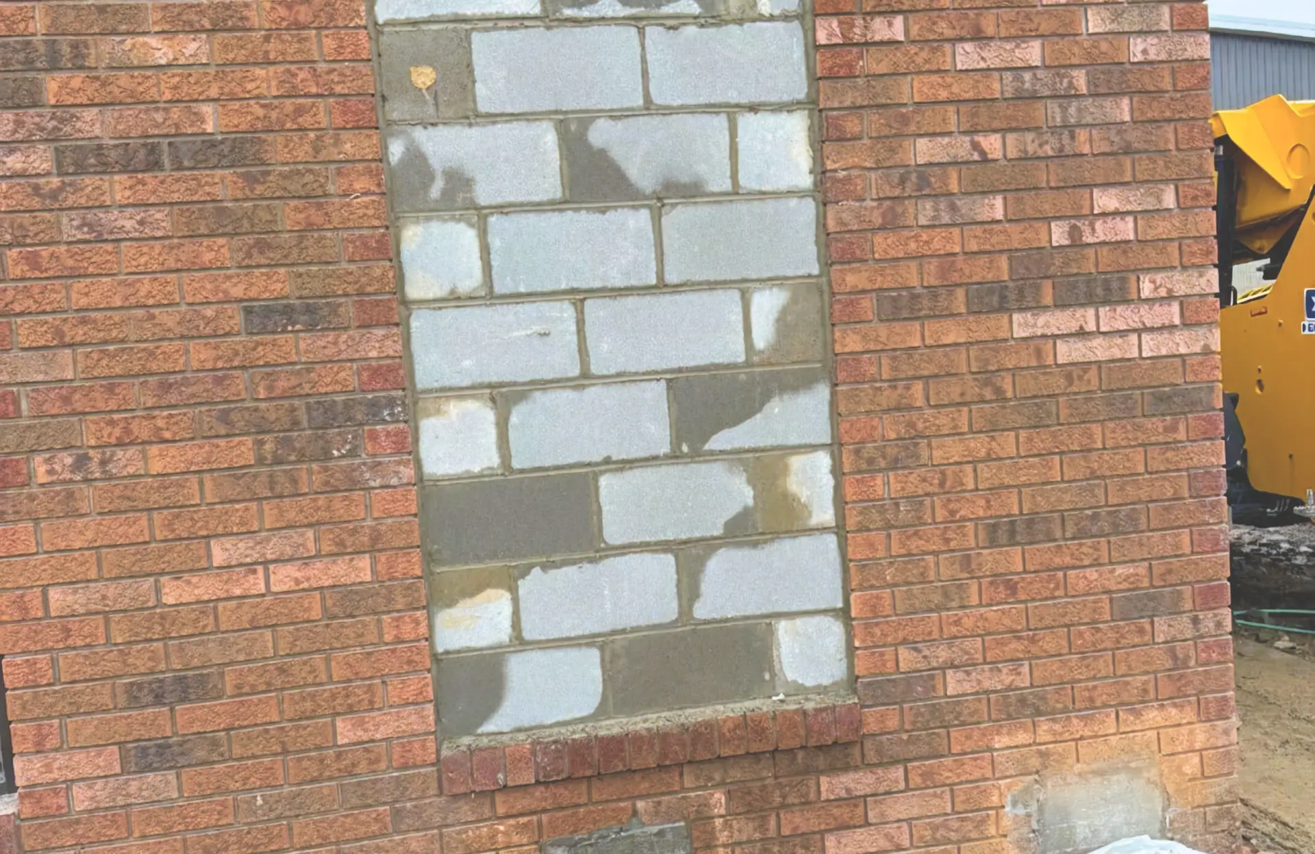 Stone Haven Developments A brick wall with a window-sized section filled in with mismatched cinder blocks and mortar, contrasting with the surrounding red bricks. Ontario