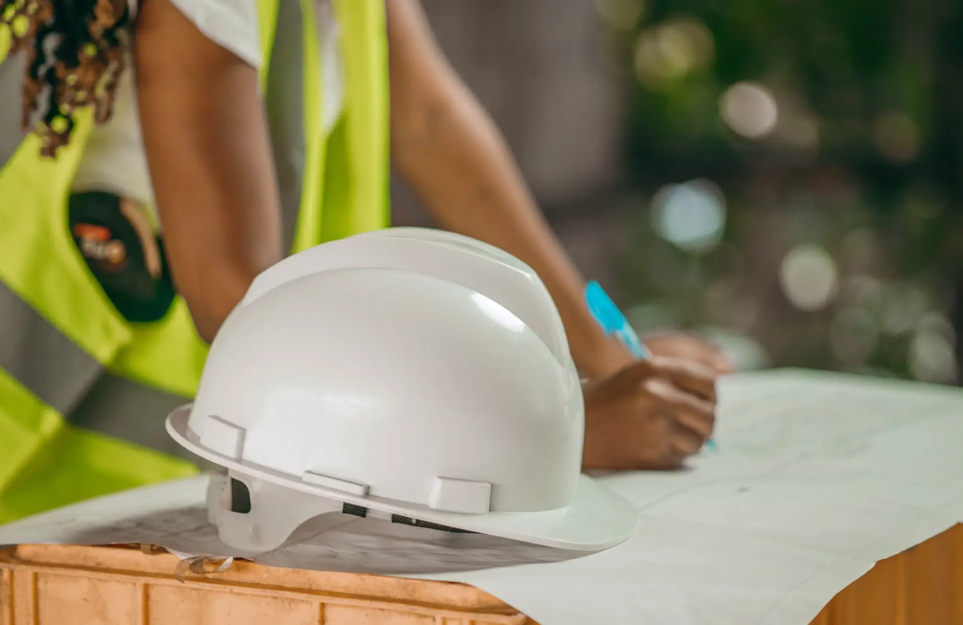 Stone Haven Developments A white construction hard hat rests on a table while a person in a reflective vest writes on a document in the background. Ontario