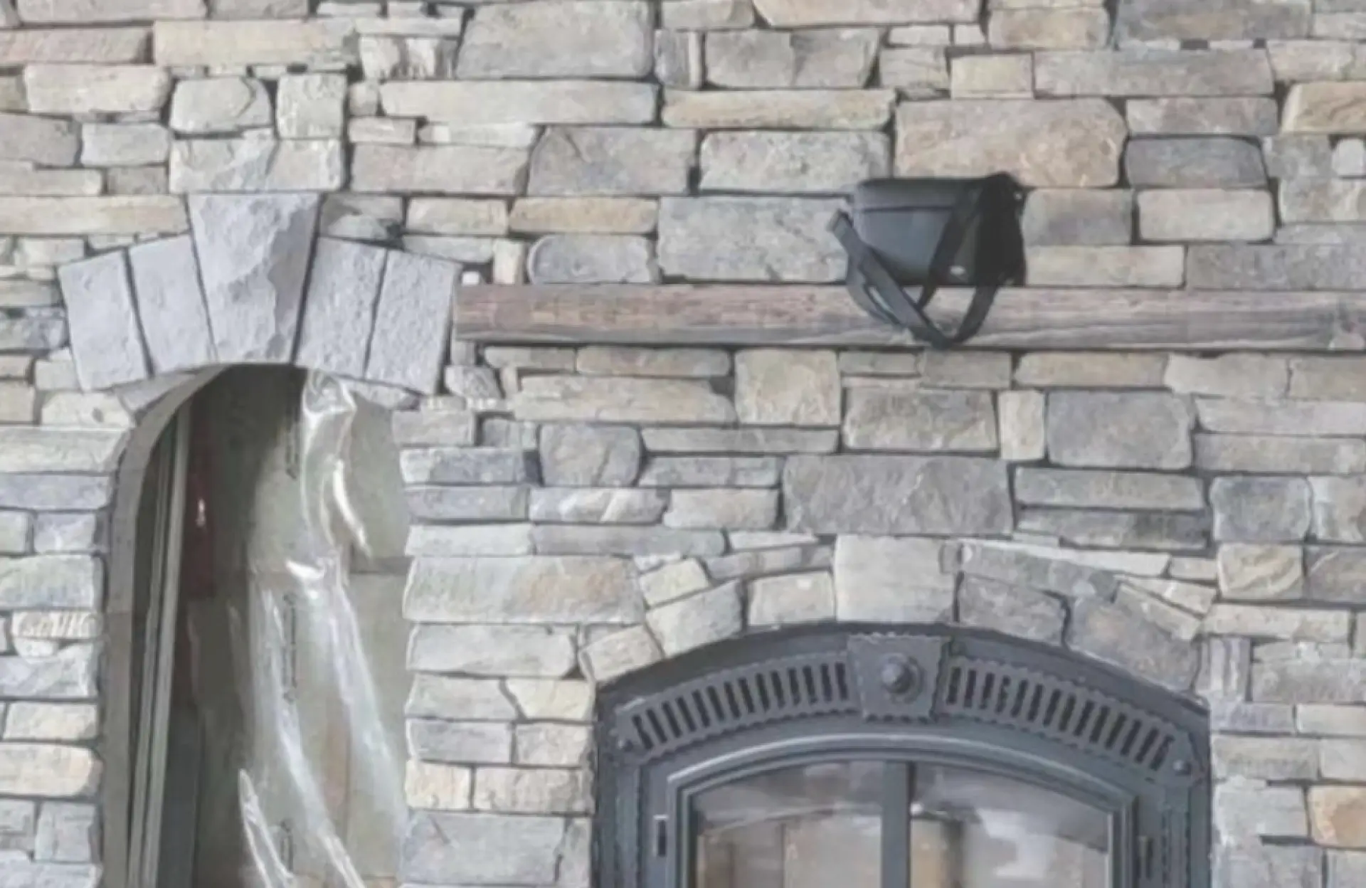 Stone Haven Developments Stone wall with an arched fireplace, a wooden mantel holding a black object, and a plastic sheet covering part of the left side. Ontario