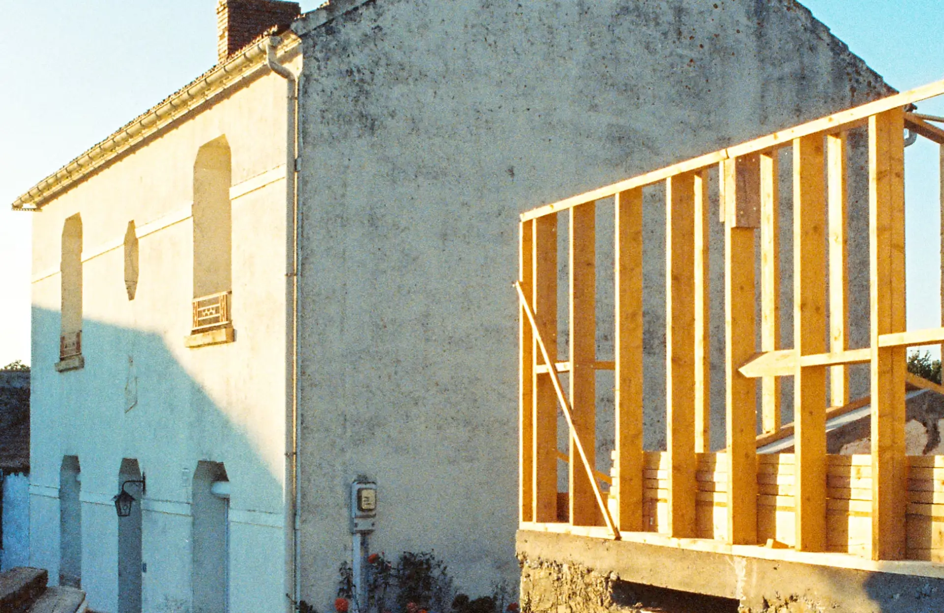 Stone Haven Developments A white stucco house with a brick chimney stands beside a wooden frame structure under construction, lit by sunlight. Ontario
