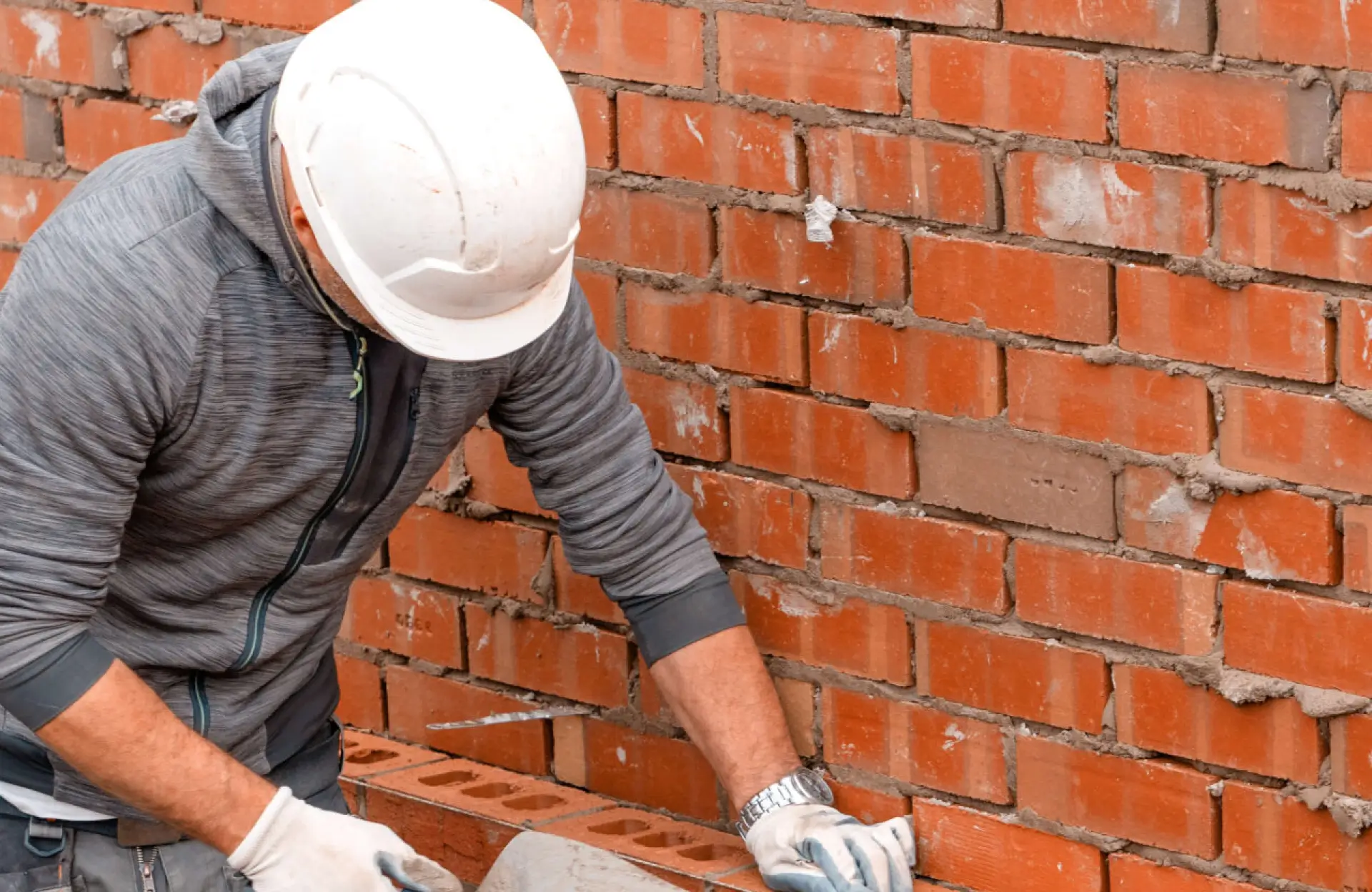 Stone Haven Developments A construction worker wearing a white hard hat and gloves lays bricks, building a brick wall. Ontario