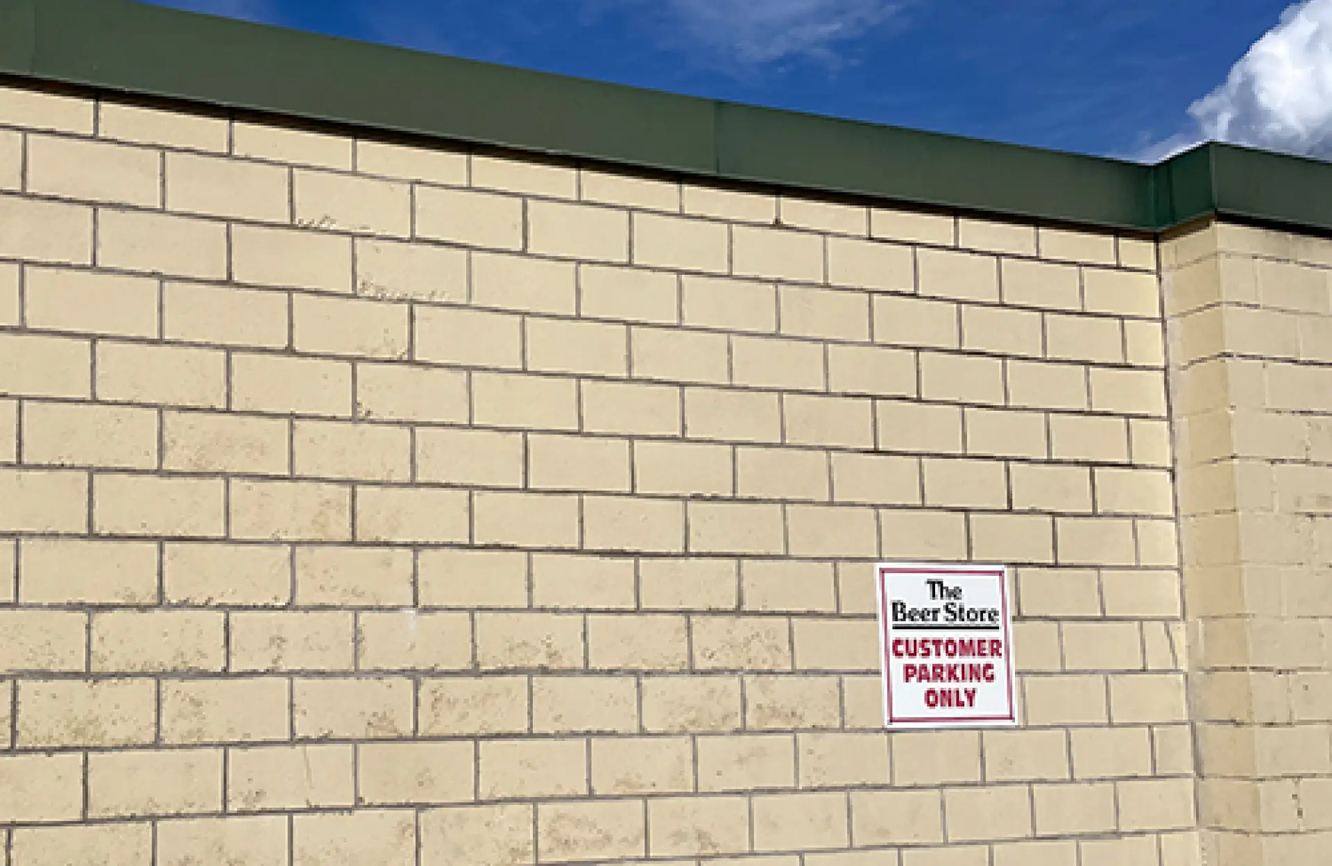 Stone Haven Developments A beige brick wall with a green roof edge, featuring a sign that reads "The Beer Store Customer Parking Only" under a blue sky. Ontario