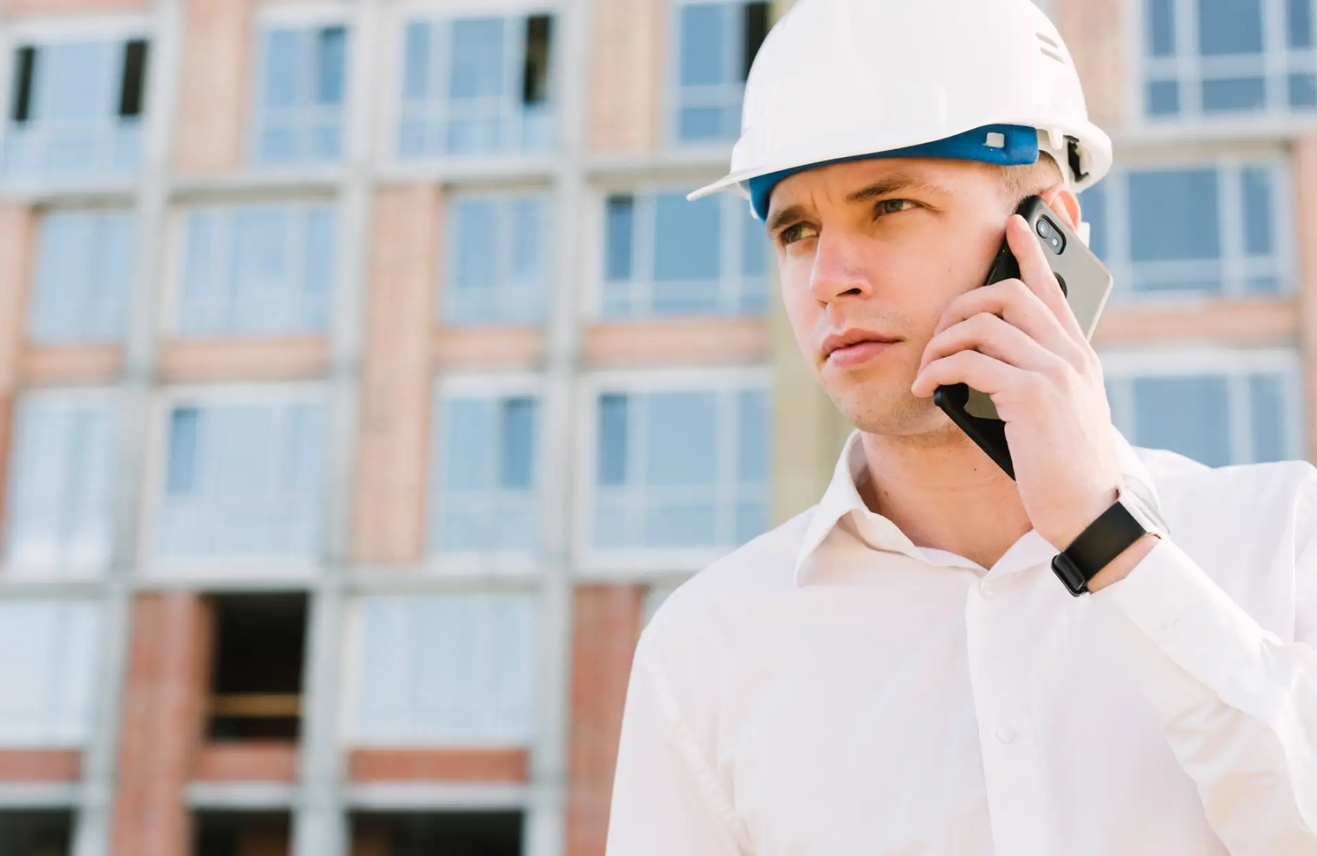 Stone Haven Developments A man wearing a white hard hat and white shirt is talking on a smartphone in front of a building under construction. Ontario