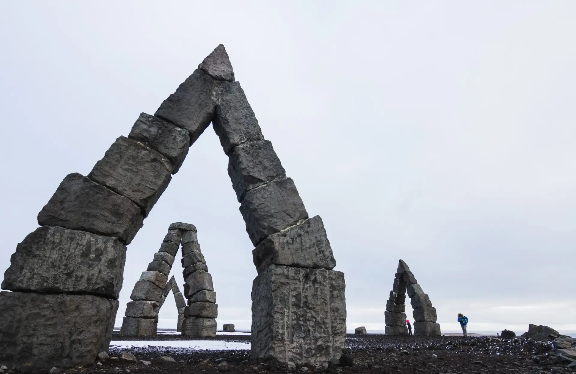 Stone Haven Developments Large stone arch structures stand on rocky ground under a cloudy sky, with two people walking in the background. Ontario