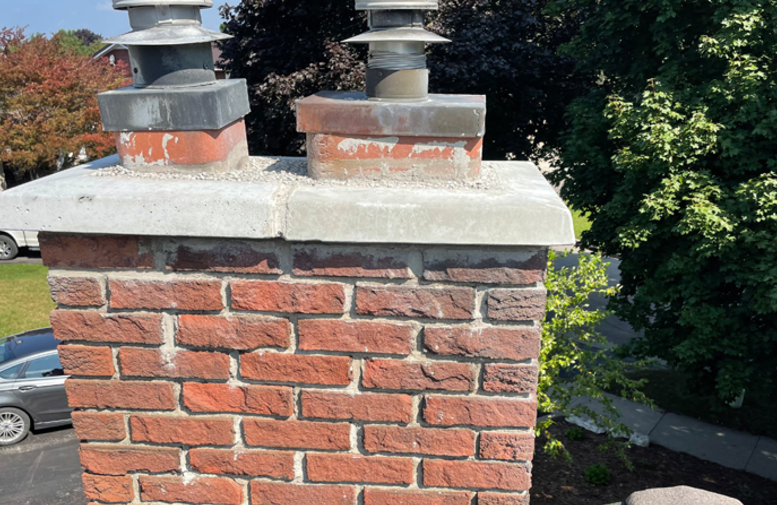 Stone Haven Developments A close-up view of a red brick chimney with two metal flue caps, set against a backdrop of trees, cars, and a residential street. Ontario