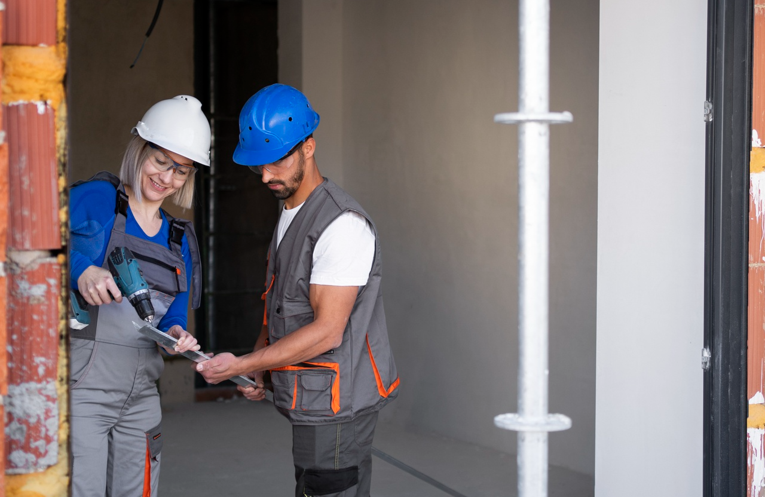 Stone Haven Developments Two construction workers, one holding a drill and the other holding papers, stand together at a building site wearing safety gear and helmets. Ontario