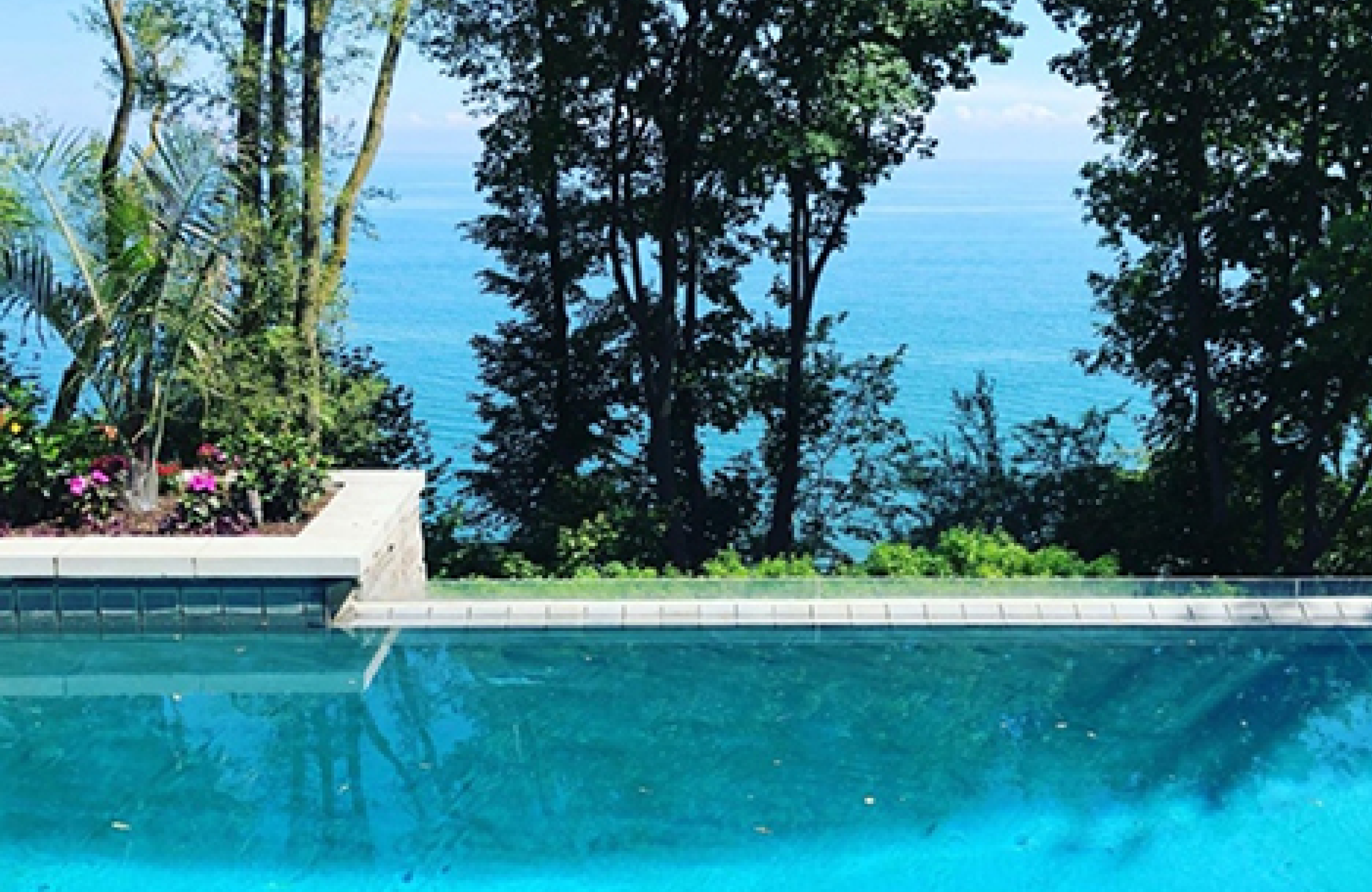 Stone Haven Developments A clear blue swimming pool in the foreground with trees and a view of the ocean in the background under a sunny sky. Ontario