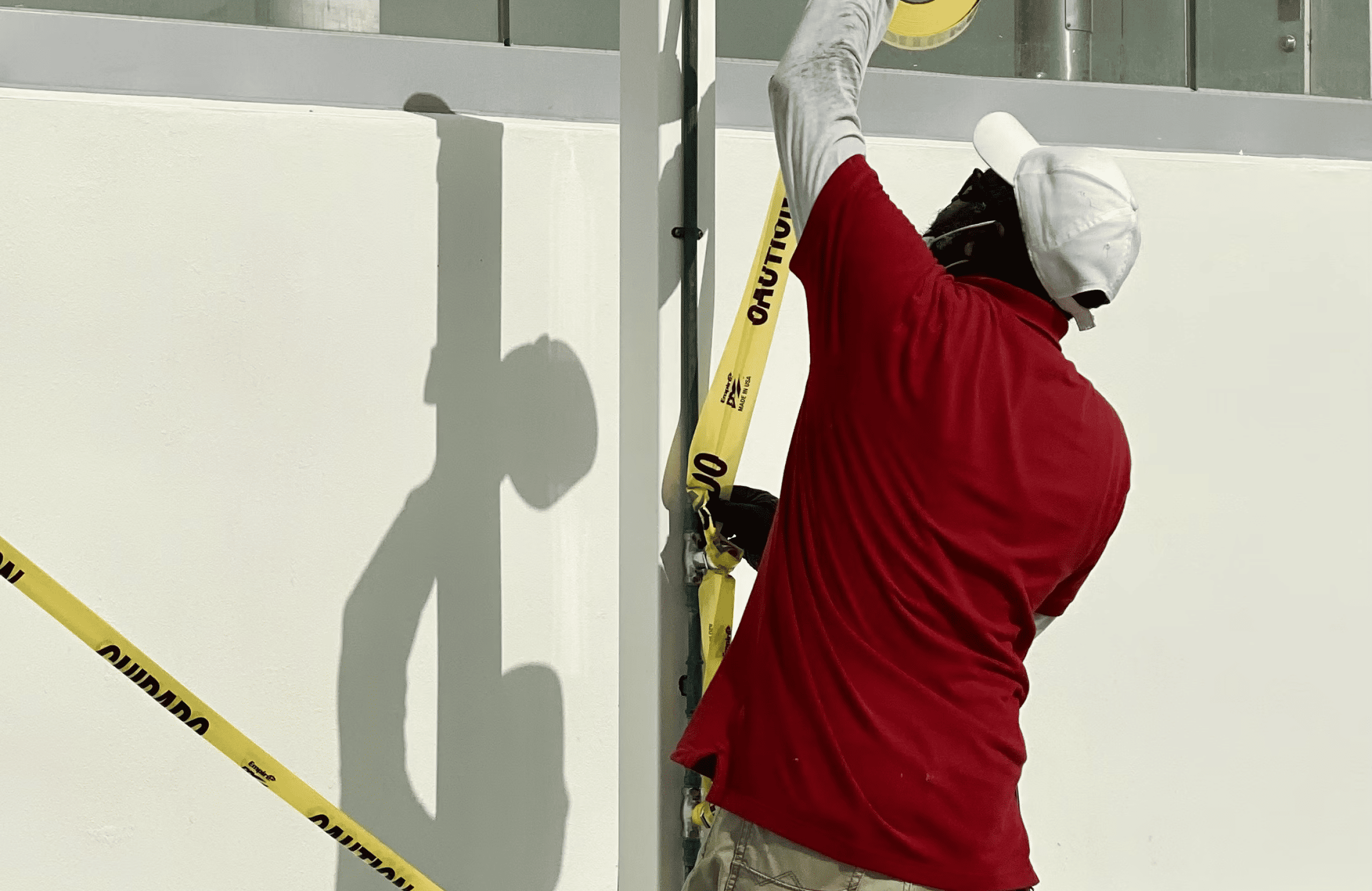 Stone Haven Developments A person wearing a red shirt and white cap secures yellow caution tape to a pole beside a white wall. Ontario