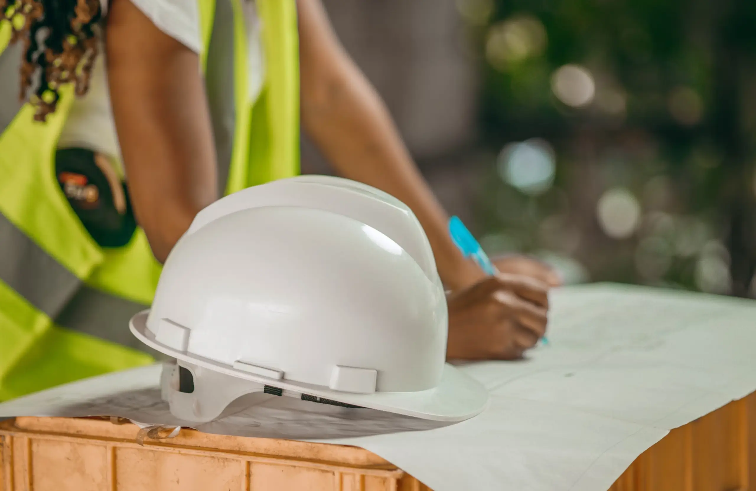 Stone Haven Developments A white safety helmet rests on a table with construction plans, while a person in a reflective vest writes in the background. Ontario
