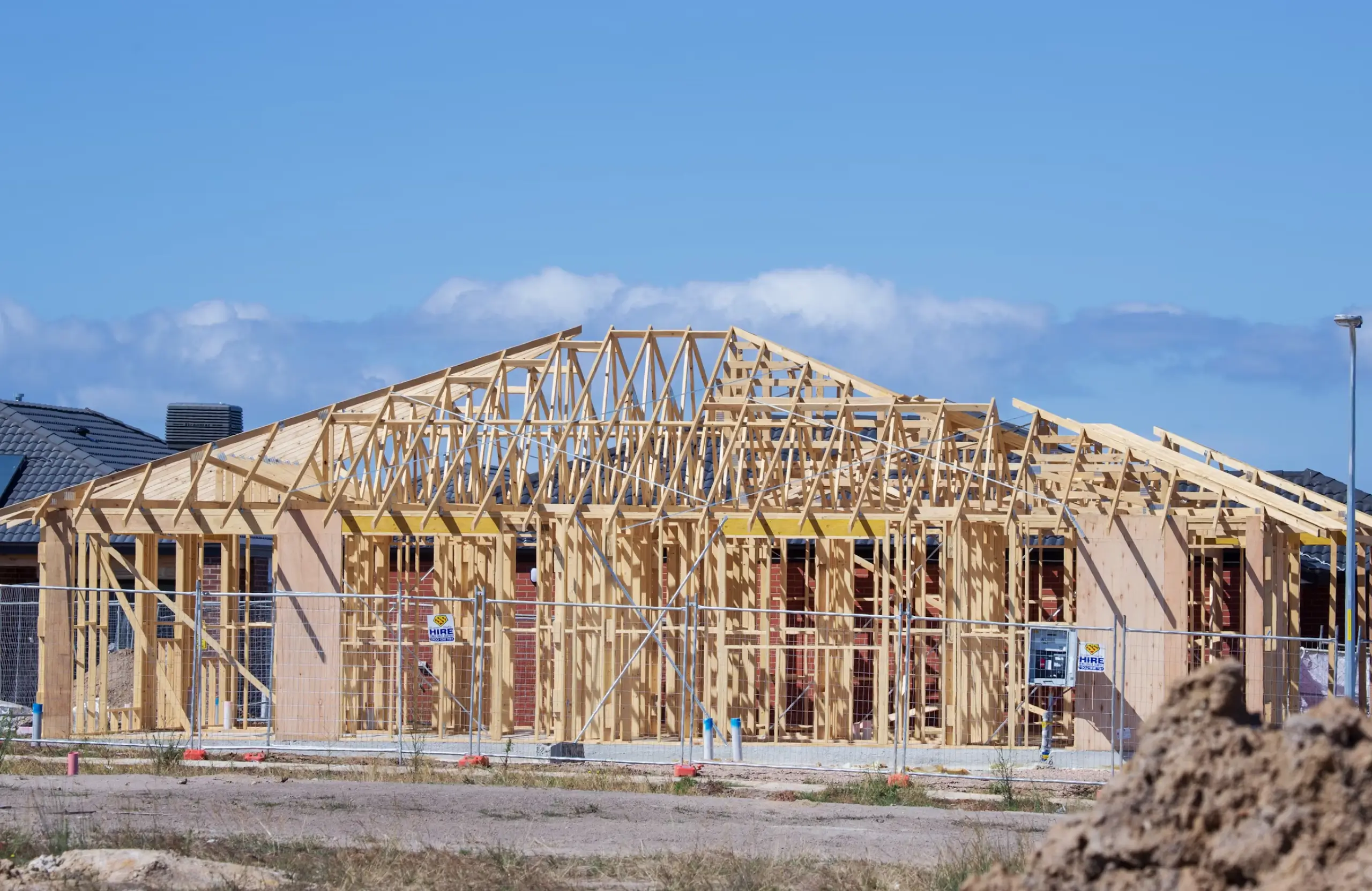 Stone Haven Developments A partially constructed house with a visible wooden frame, roof trusses, and exterior walls, set behind a temporary metal fence under a clear blue sky. Ontario