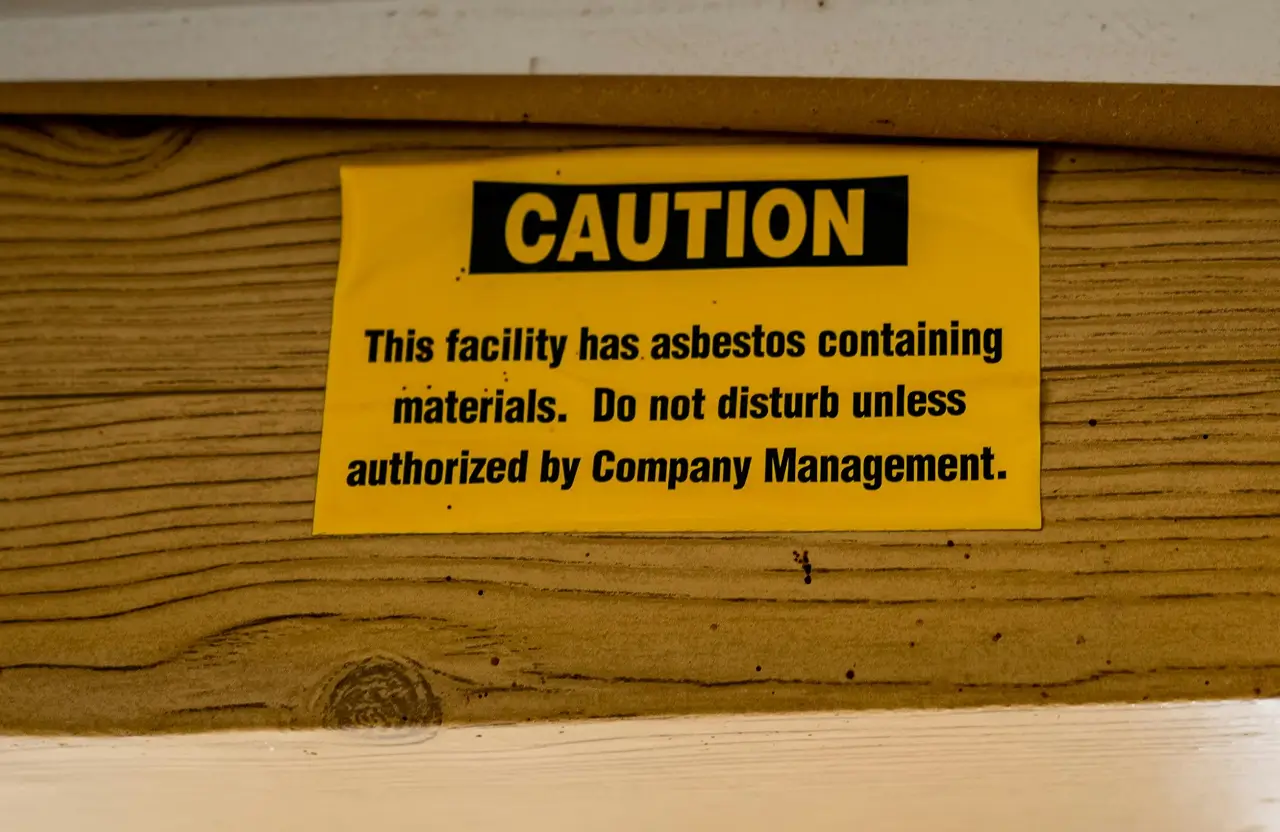 Stone Haven Developments Yellow caution sign on wood states asbestos is present; do not disturb materials unless authorized by company management. Ontario