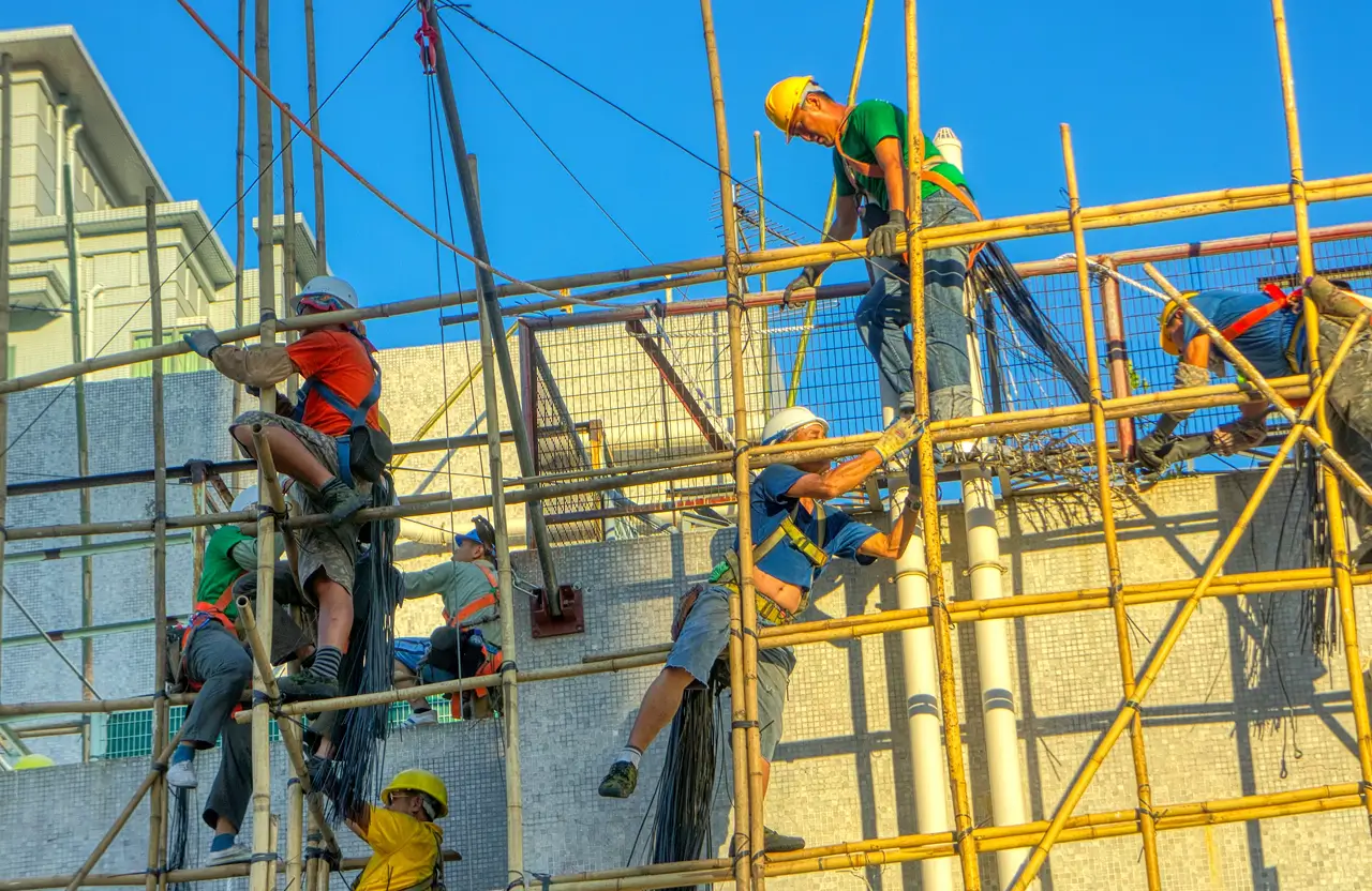 Stone Haven Developments Five construction workers wearing safety gear assemble and climb bamboo scaffolding against a building with a clear blue sky in the background. Ontario