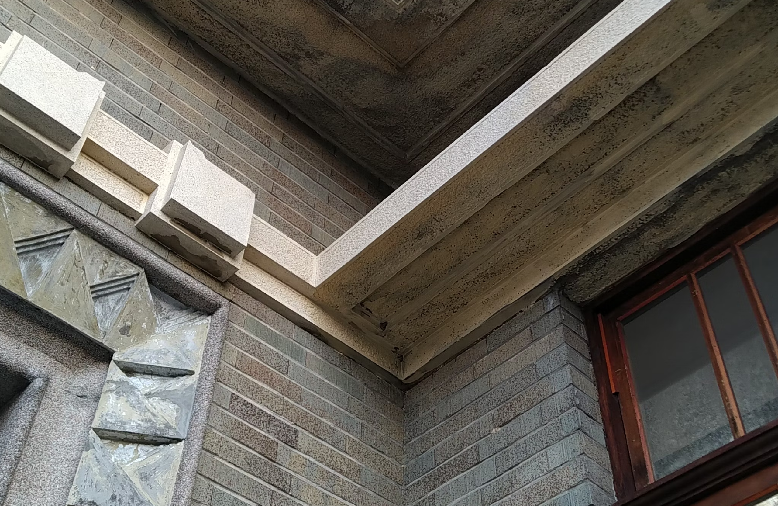 Stone Haven Developments Close-up of a building corner showing textured grey brick walls, a section of a window with a wooden frame, and geometric stone details near the ceiling. Ontario