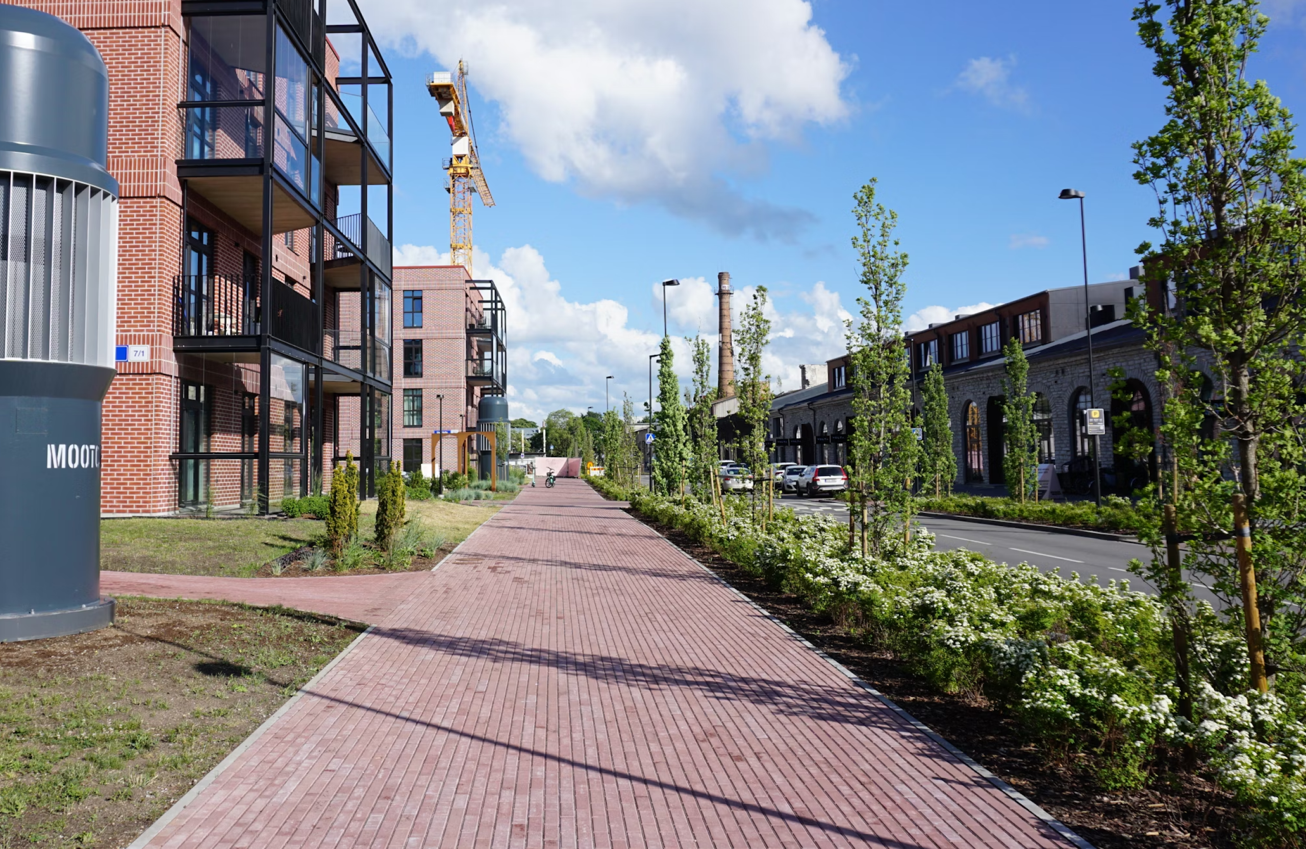 Stone Haven Developments A modern brick apartment building and construction crane stand beside a wide pedestrian path lined with young trees and bushes on a sunny day. Ontario