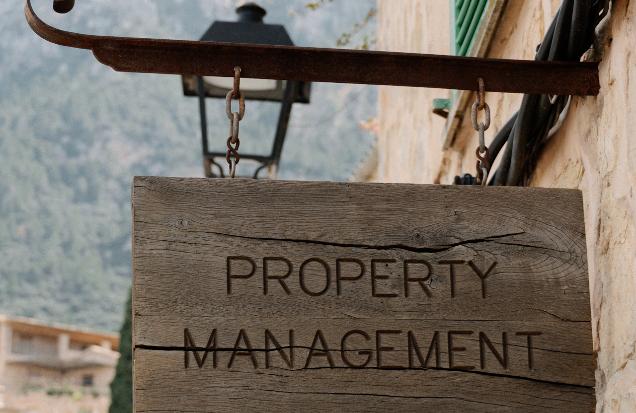 Stone Haven Developments A wooden sign reading "Property Management" hangs outside a building, with a lantern and mountains visible in the background. Ontario