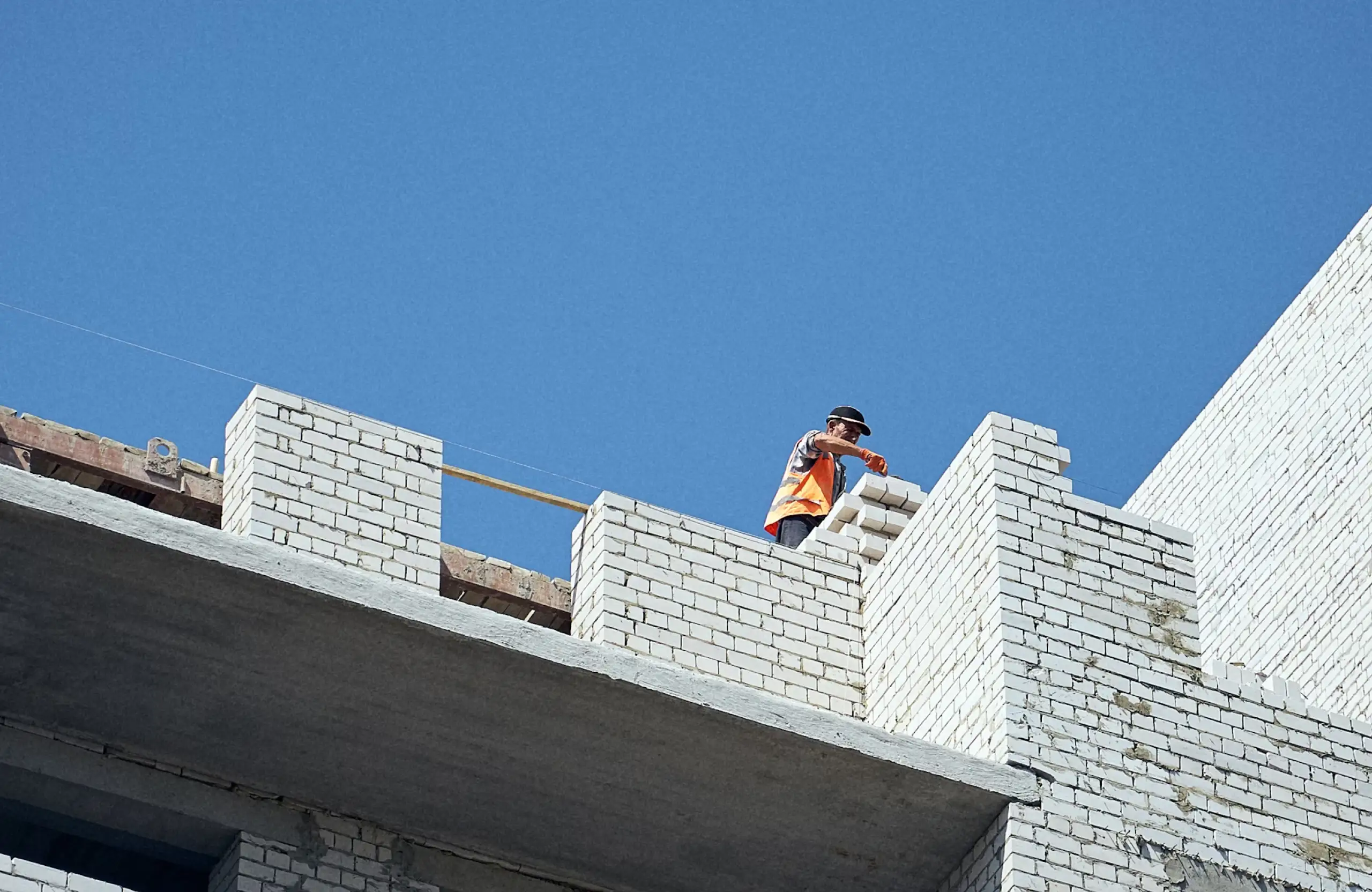Stone Haven Developments A construction worker in an orange vest is building a white brick wall on the upper floor of a building under a clear blue sky. Ontario