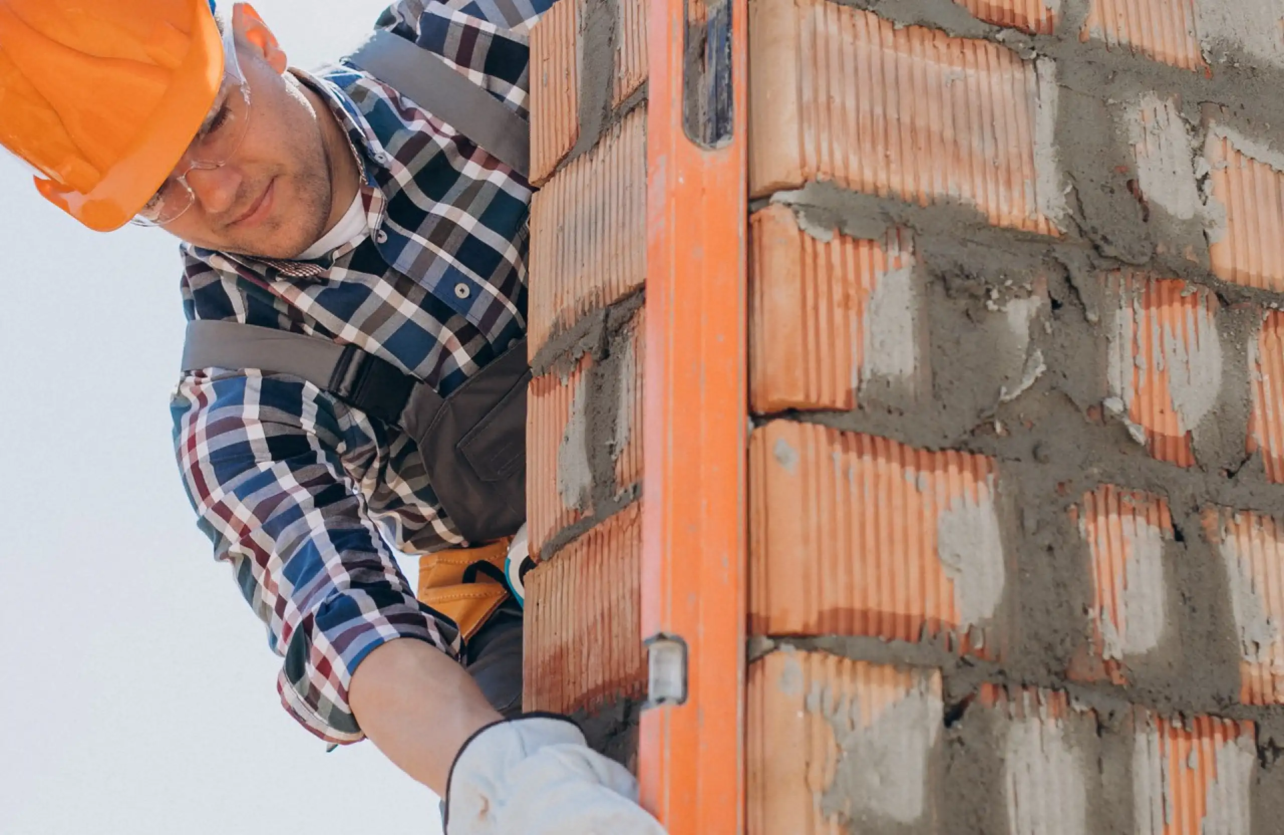 Stone Haven Developments A construction worker in a plaid shirt and orange helmet uses a spirit level to check the alignment of a brick wall. Ontario