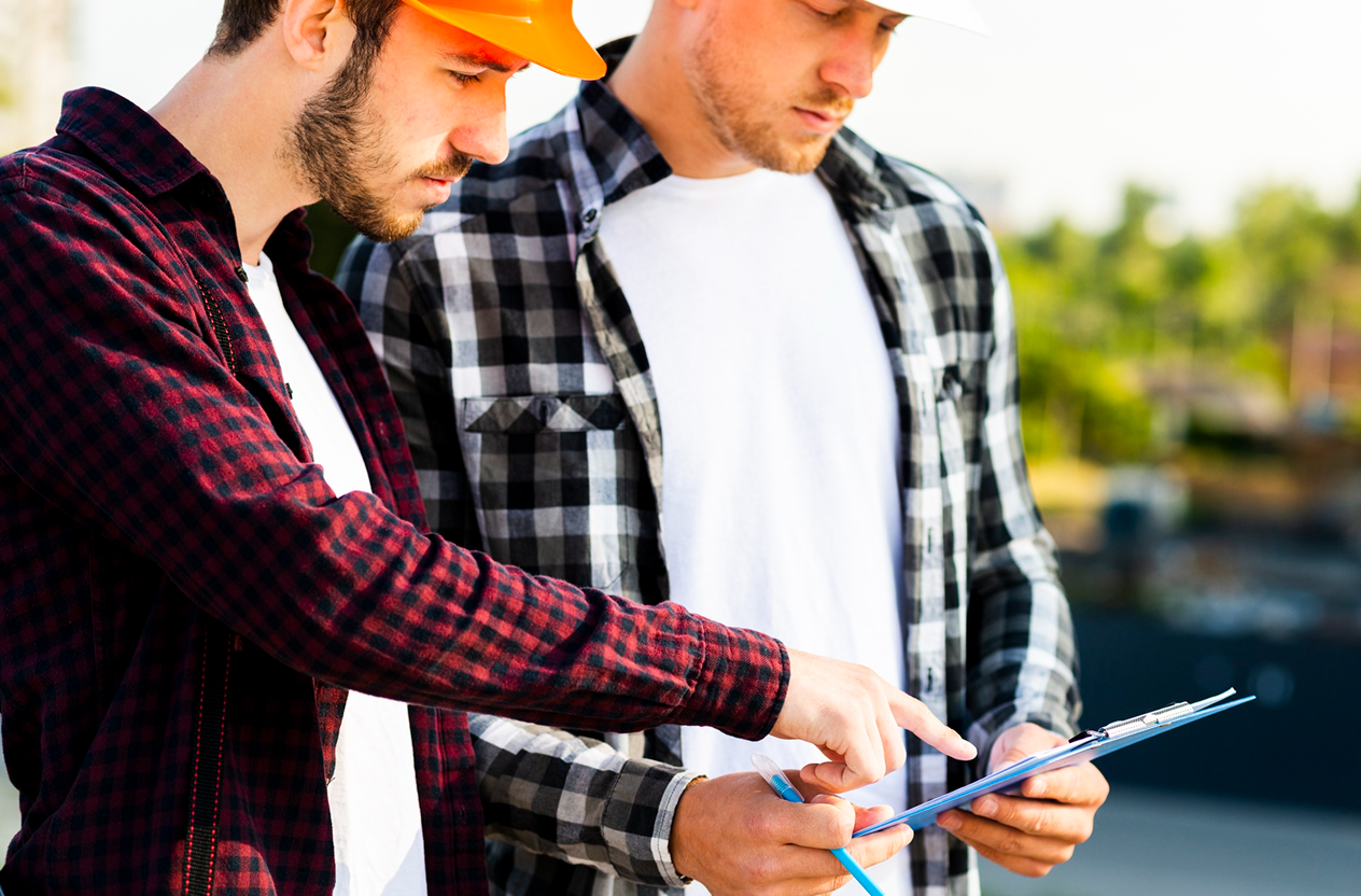 Stone Haven Developments Two men in plaid shirts and hard hats review documents on a clipboard outdoors. One man is pointing at the paper while the other looks on attentively. Ontario