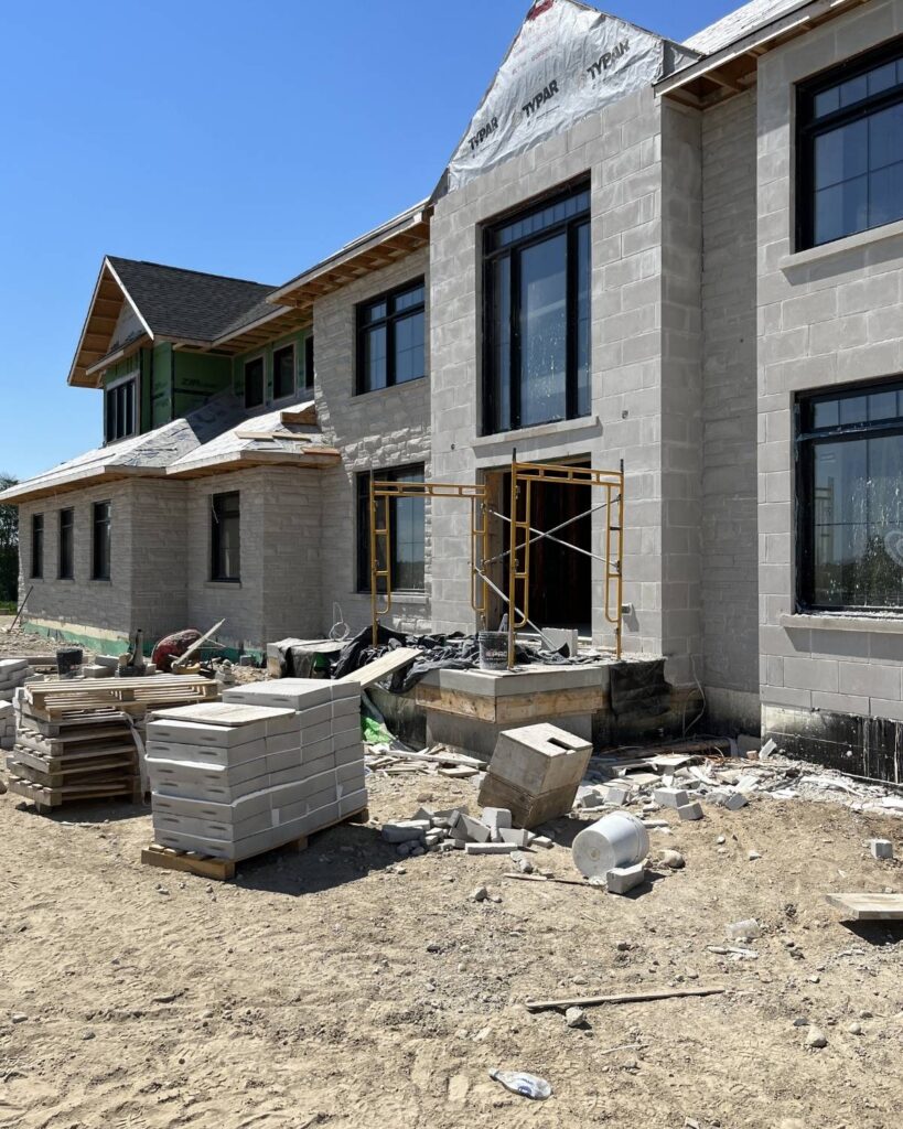Stone Haven Developments A large house under construction with exposed concrete blocks, scaffolding by the windows, building materials, and debris scattered on the ground. Ontario