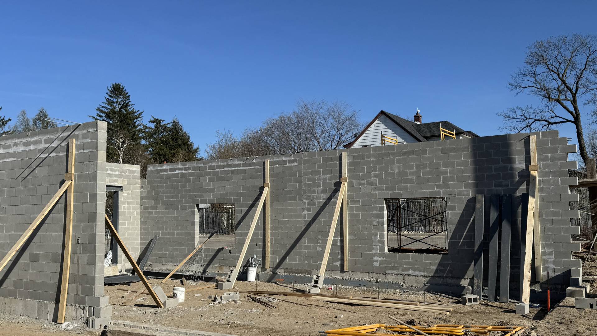 Stone Haven Developments Partially constructed cinder block building with wooden supports, open window spaces, scattered construction materials, and a house visible in the background under a clear sky. Ontario