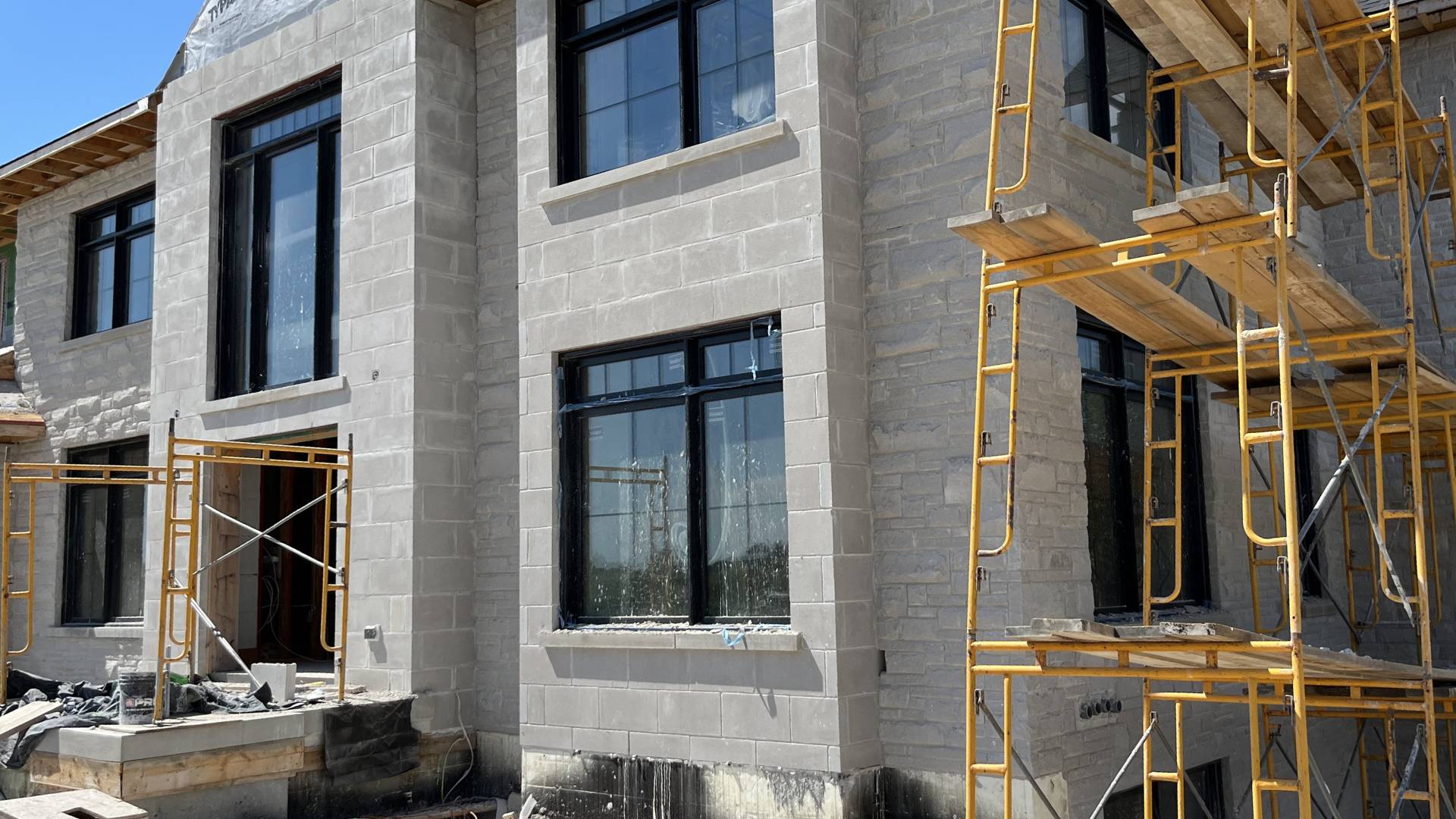 Stone Haven Developments A modern two-story house under construction with large black-framed windows, scaffolding, and unfinished exterior walls. Ontario