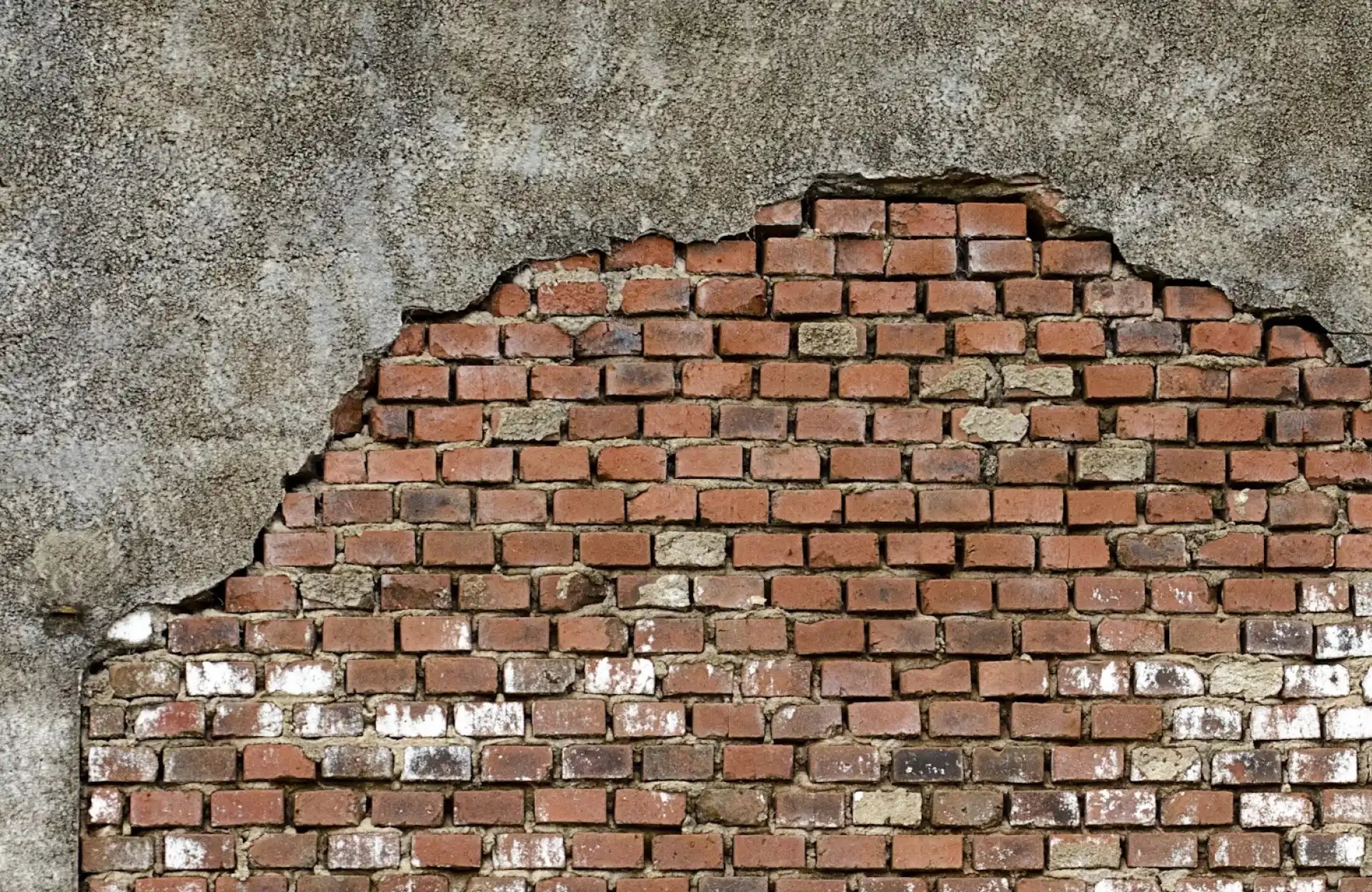 Stone Haven Developments Exposed red brick wall with cracked and crumbling gray plaster partially covering the upper section. Ontario