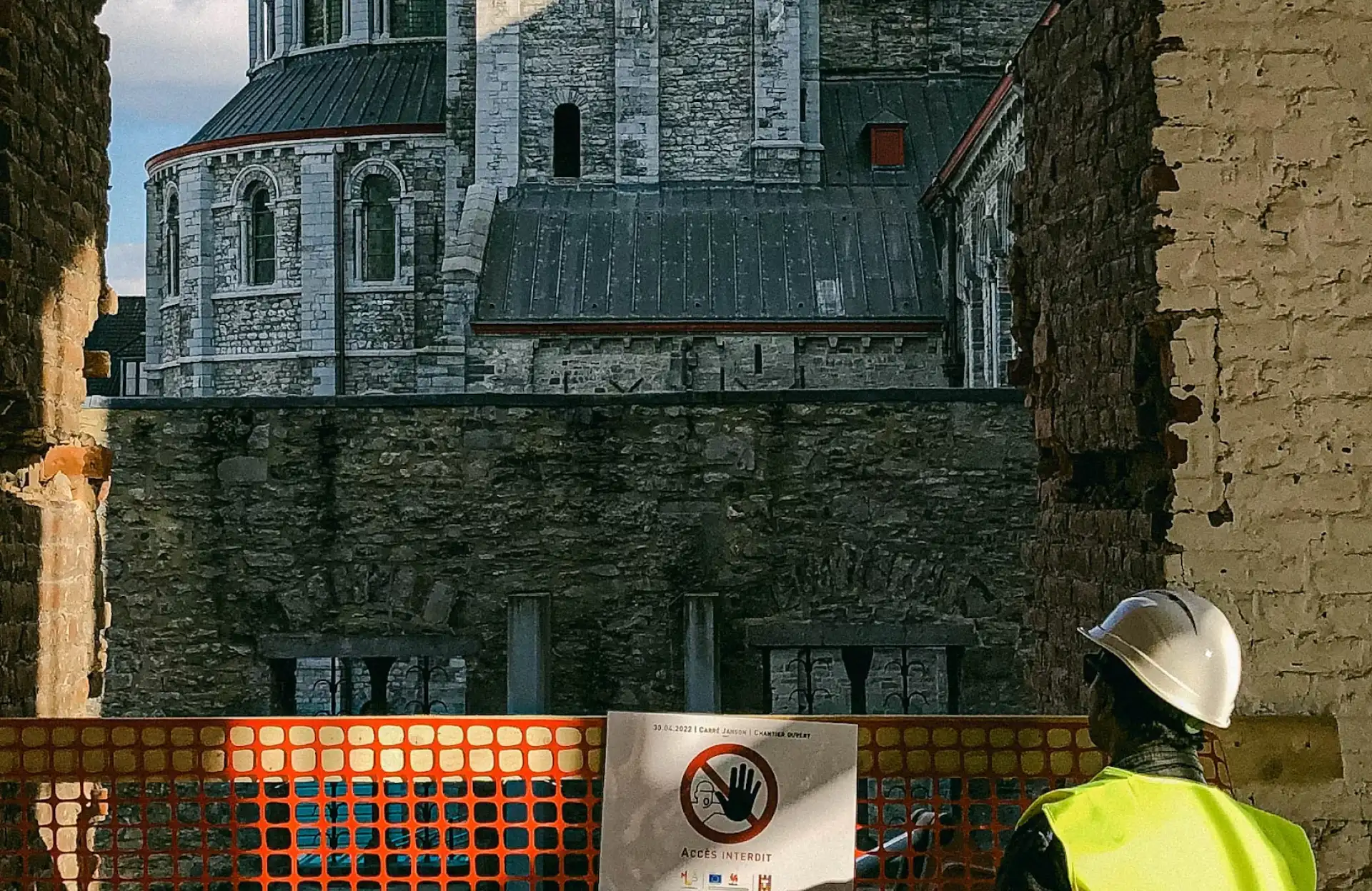 Stone Haven Developments A construction worker in a hard hat and vest looks at a historic stone building through a gap in a brick wall, with a no entry sign on an orange barricade. Ontario