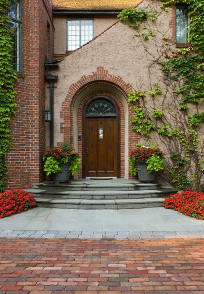 Stone Haven Developments A wooden arched front door with a fanlight window, surrounded by ivy-covered brick and stucco walls, potted plants, and red flowers on stone steps. Ontario