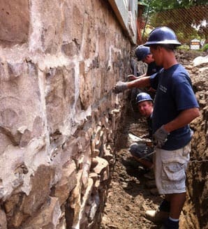 Stone Haven Developments Three construction workers in safety helmets repair or inspect a stone foundation wall at an outdoor work site. Ontario