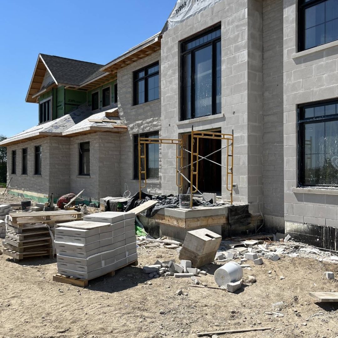 Stone Haven Developments A large house under construction with exposed cinder blocks, scaffolding near the windows, and construction materials scattered on the ground. Ontario