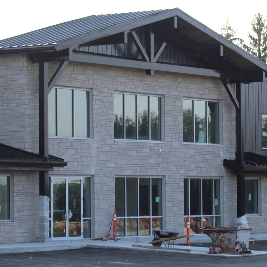 Stone Haven Developments Modern two-story commercial building with stone and metal exterior, large windows, and construction equipment and caution signs in front. Ontario
